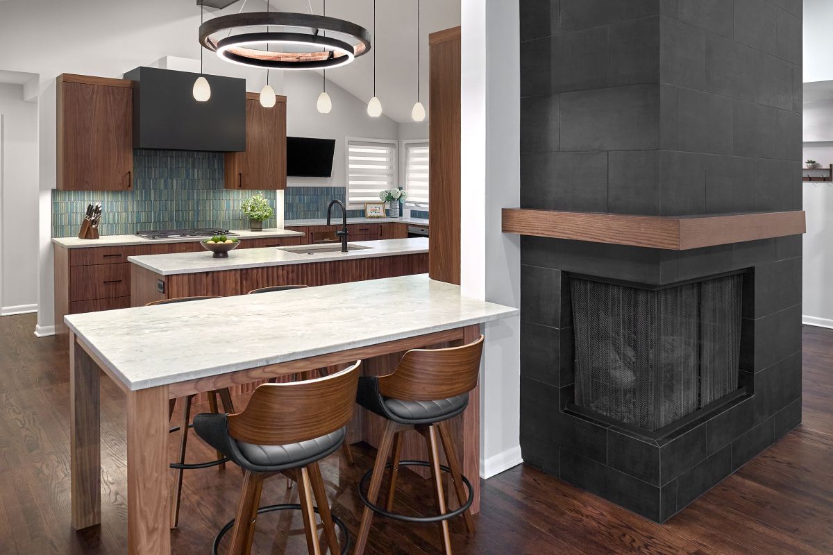 An open-concept kitchen and living area features dark wood floors, a kitchen with wood cabinets and a blue tile backsplash, and a black tiled fireplace.