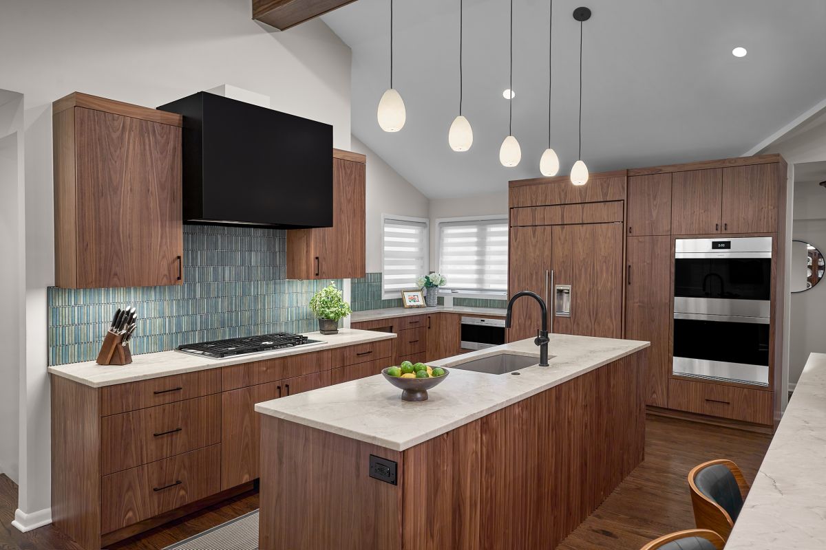 A kitchen with dark wood cabinetry, light countertops, a black range hood, and a kitchen island with a sink.