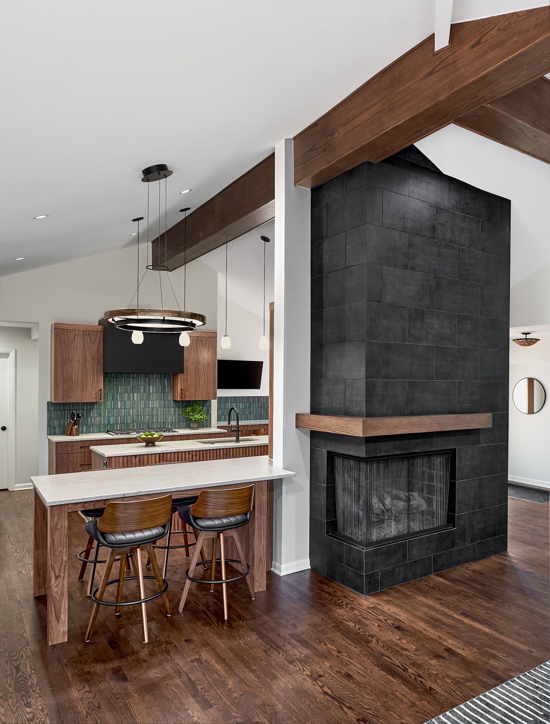 An open-concept living space features a kitchen with a dining island and a dark tiled fireplace with a wooden mantel.