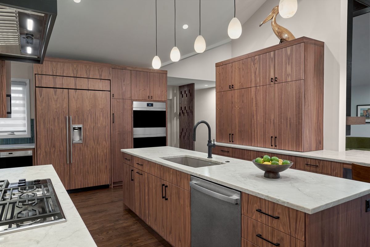 A kitchen with dark wood cabinetry, white countertops, stainless steel appliances, and pendant lights over an island.