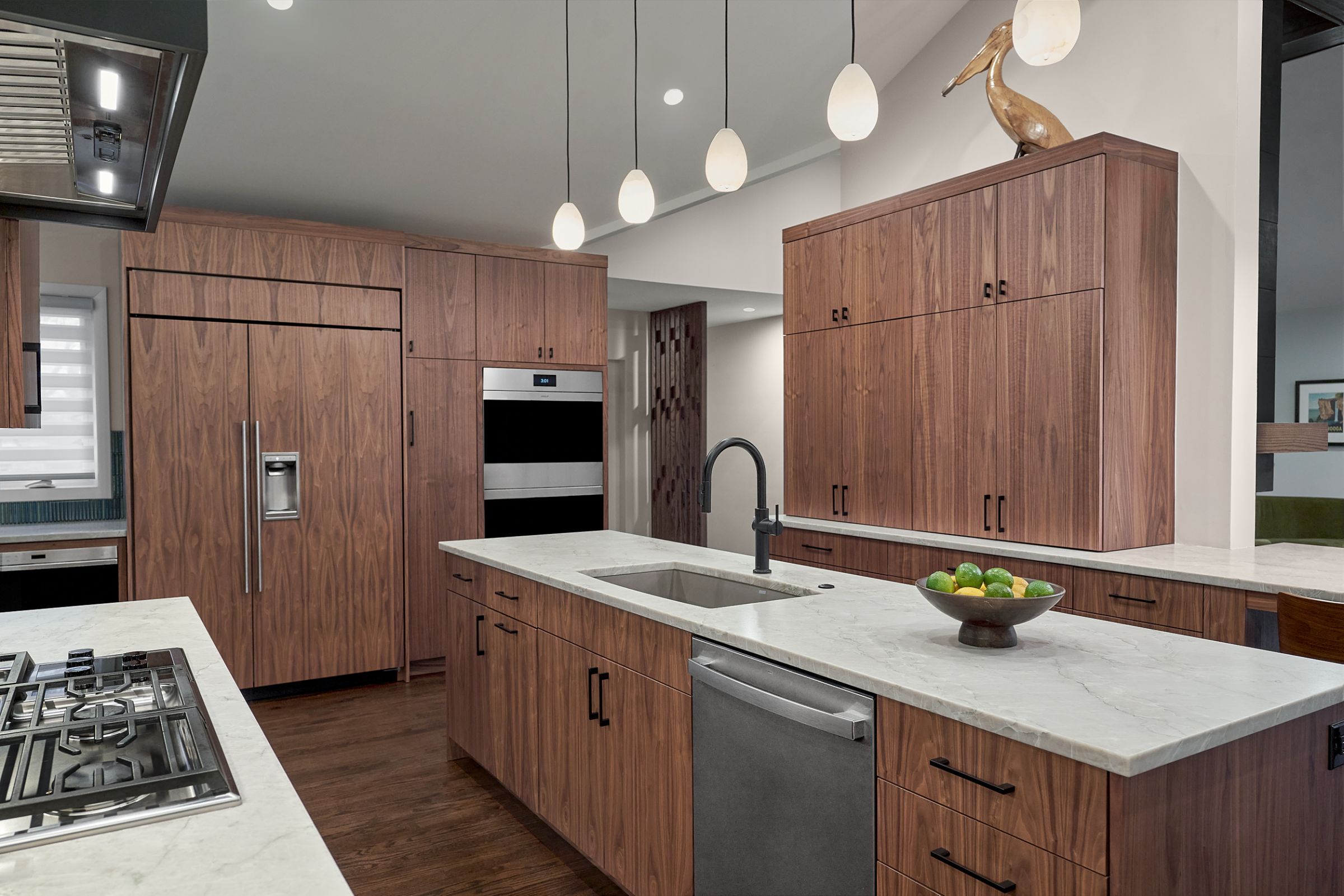 A kitchen with dark wood cabinetry, white countertops, stainless steel appliances, and pendant lights over an island.