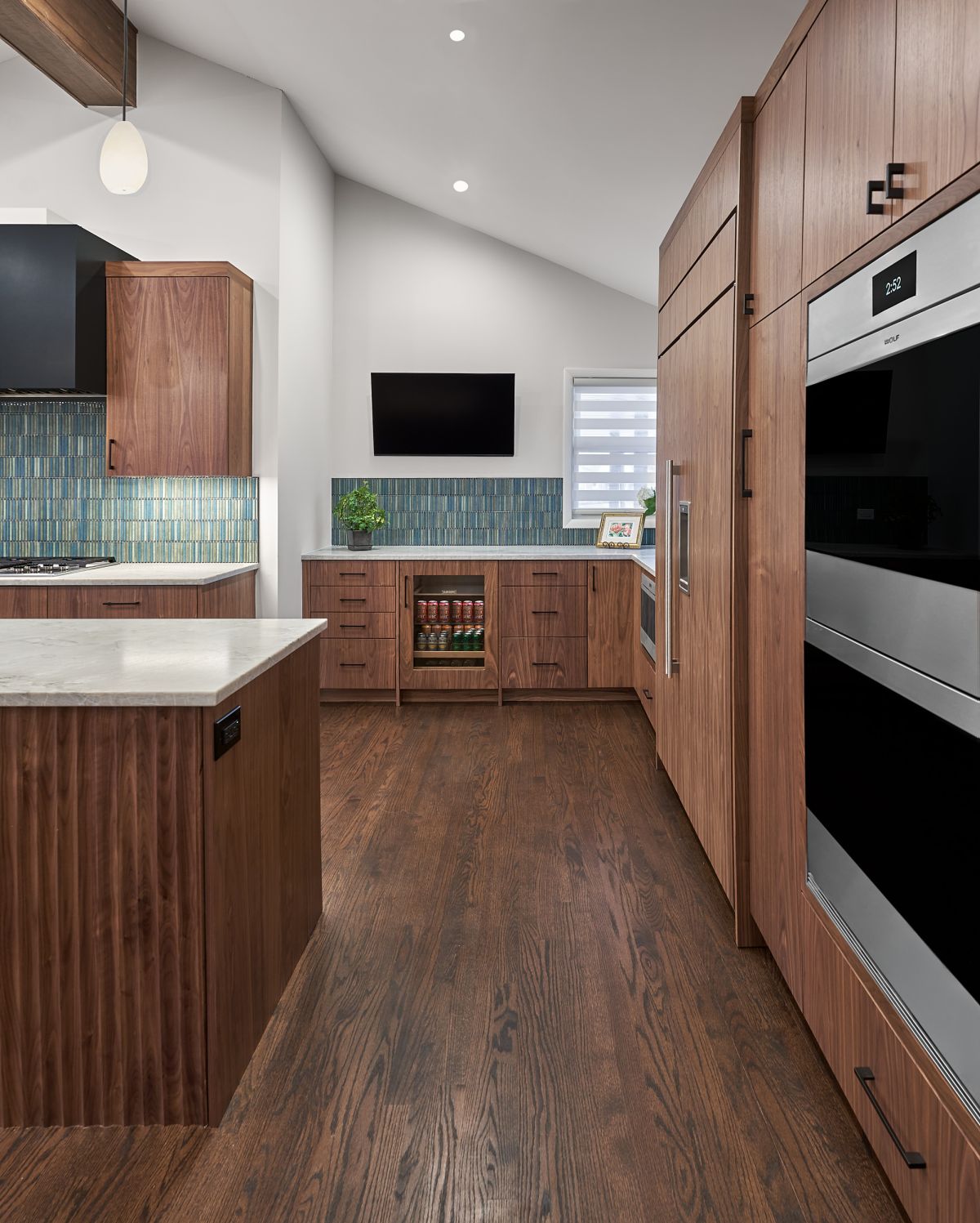 A kitchen with dark wood cabinetry, a white countertop island, a blue tiled backsplash, and dark wood floors.