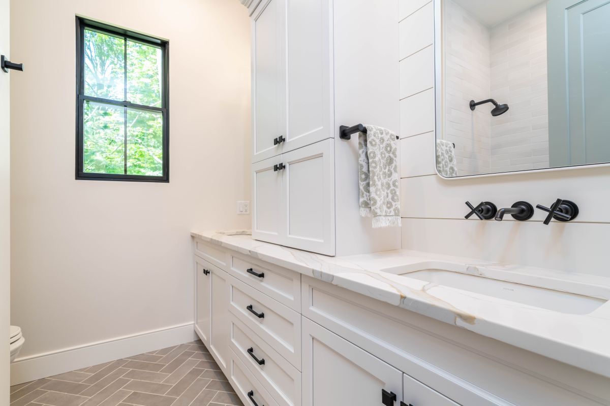 A modern farmhouse bathroom with white vanity cabinets, a white marble countertop, a wall-mounted faucet, and a large mirror.