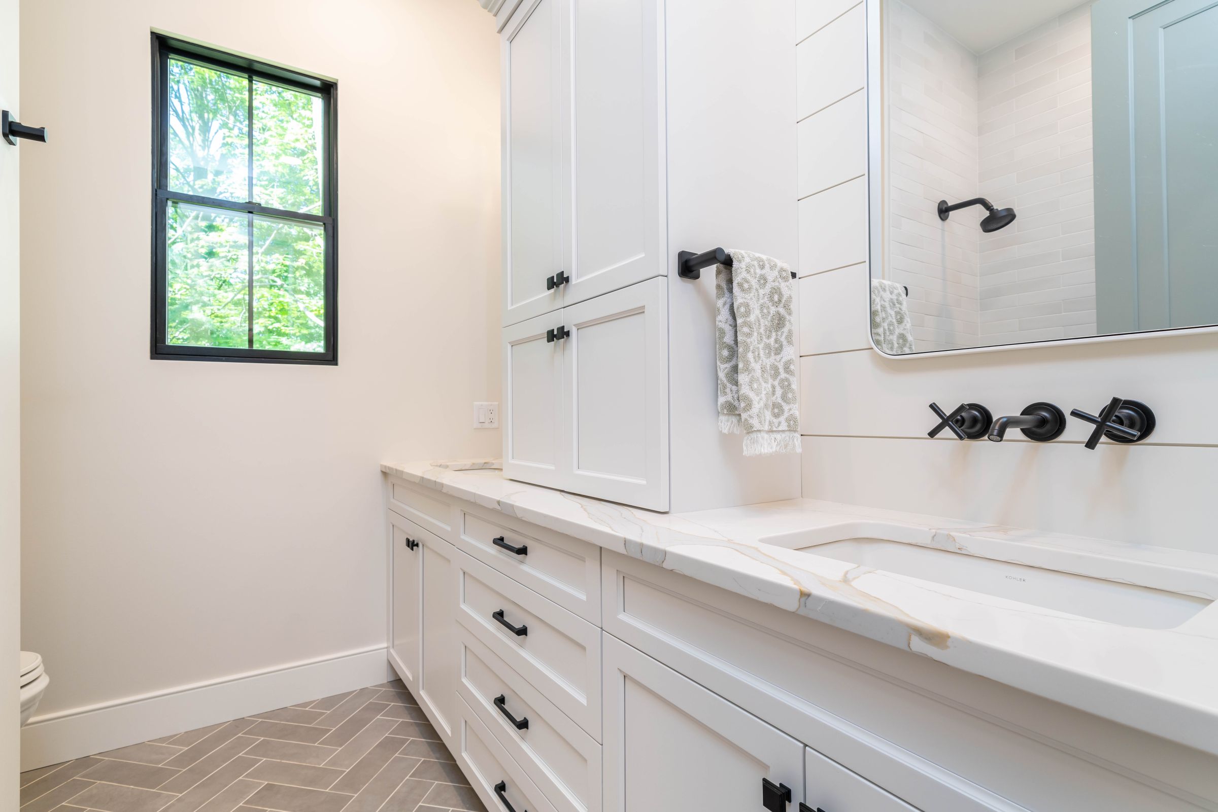 A modern farmhouse bathroom with white vanity cabinets, a white marble countertop, a wall-mounted faucet, and a large mirror.
