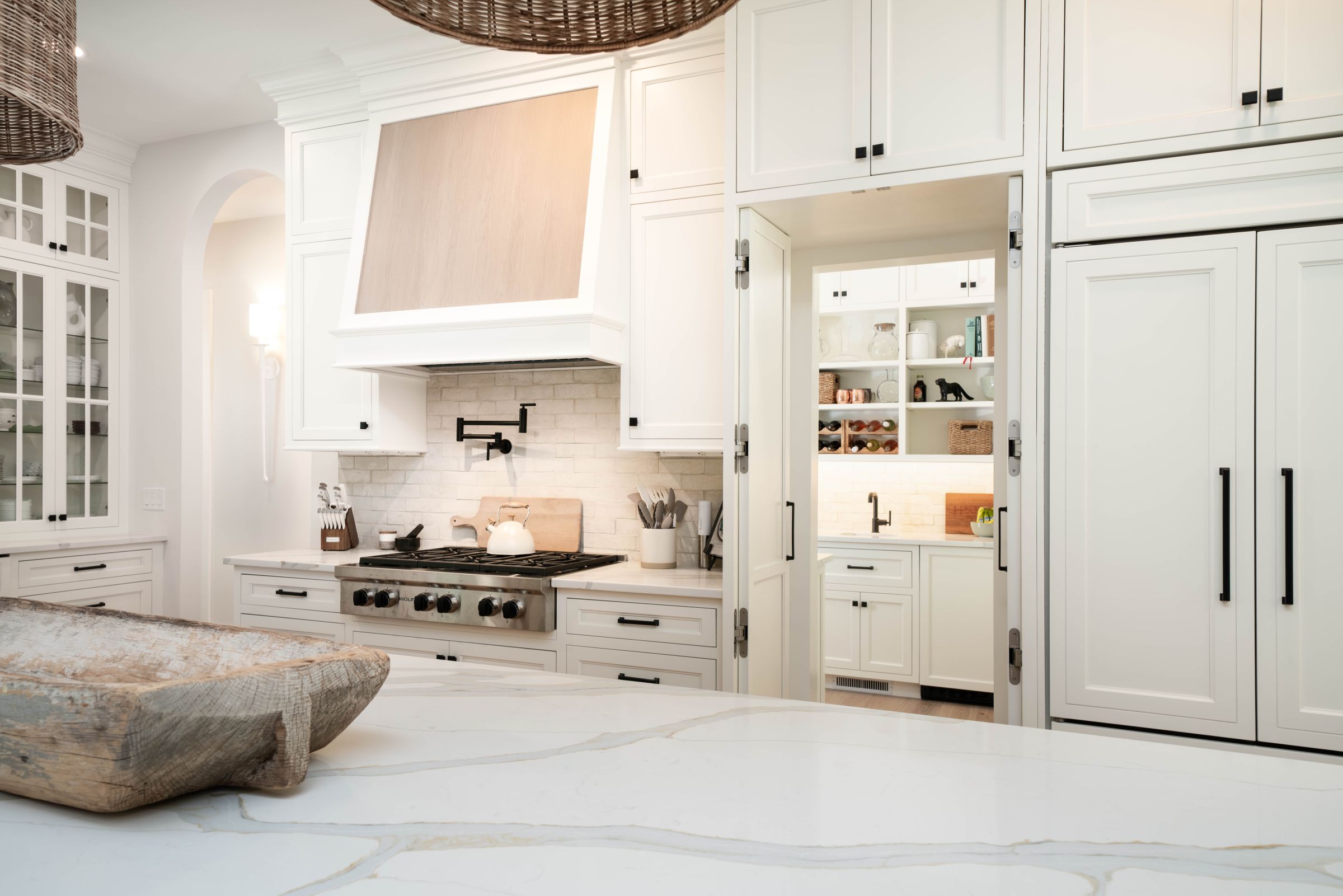 A white kitchen with a large island, a range with a pot filler, and a hidden pantry behind cabinet doors.