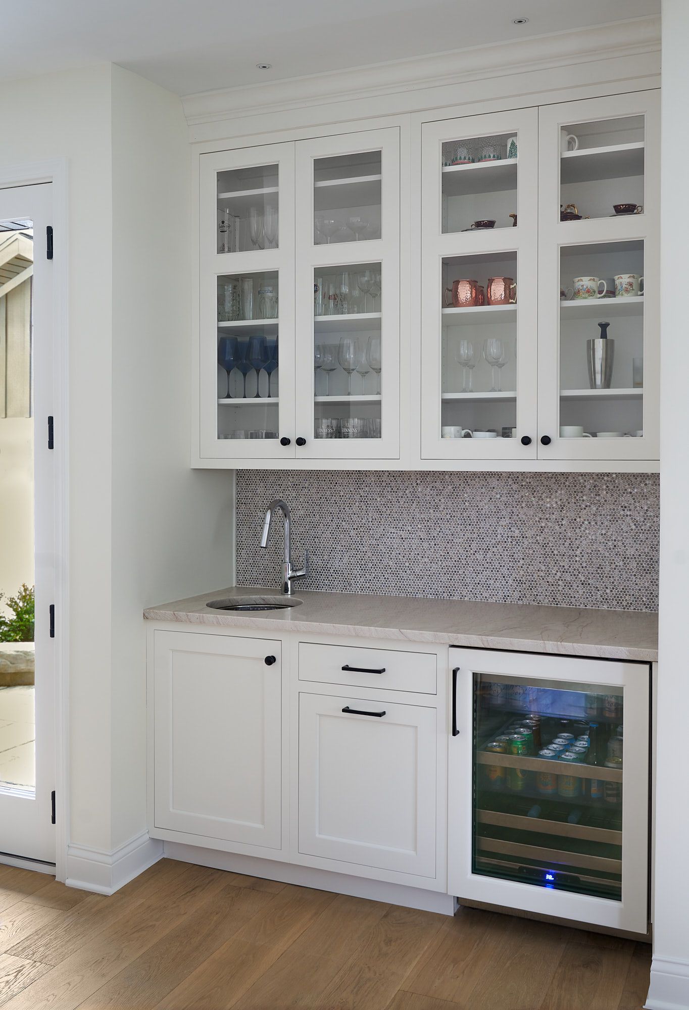 A white built-in wet bar features upper glass-front cabinets, a small sink, and a beverage refrigerator.