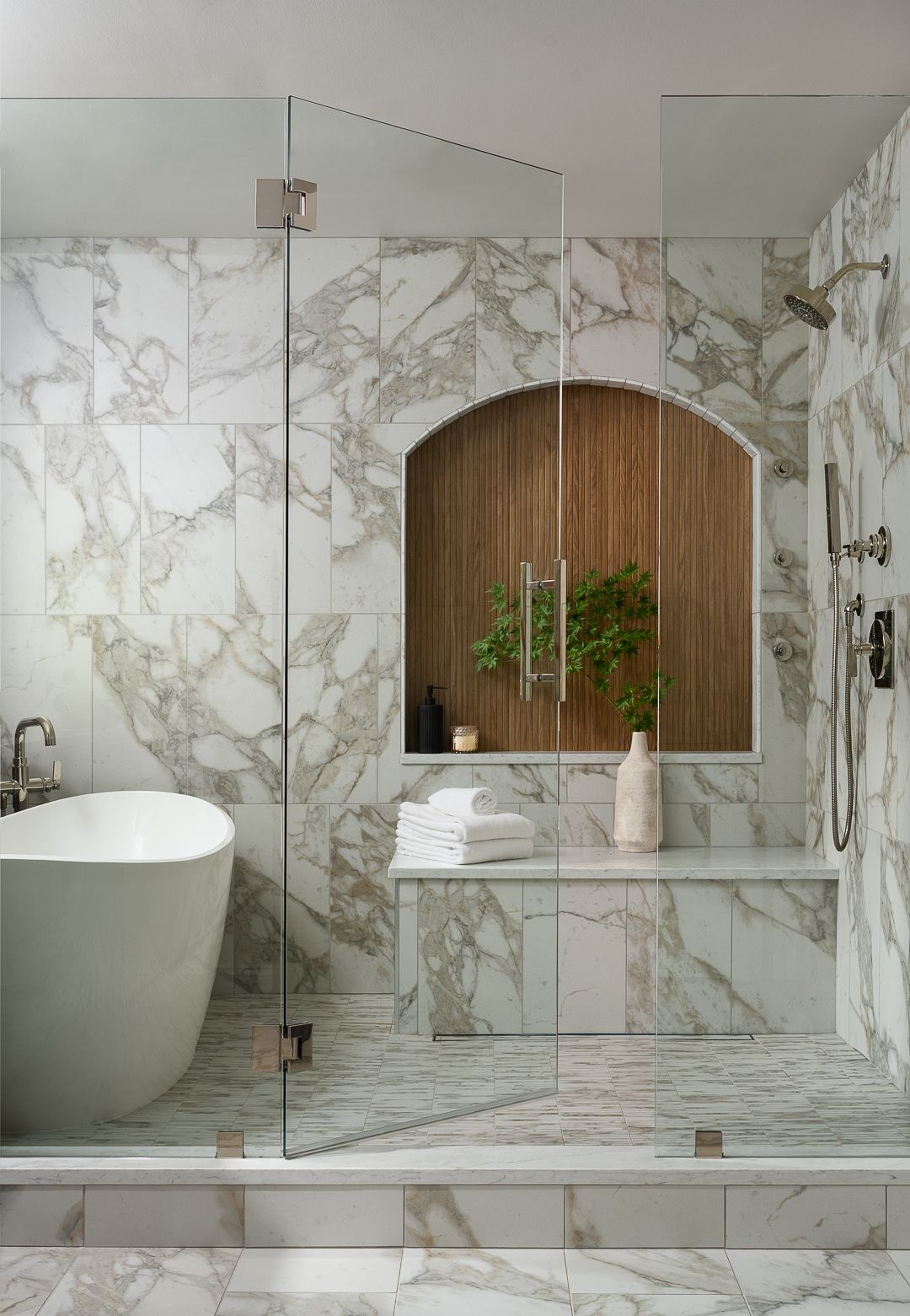 A luxurious primary bathroom features a freestanding tub and a spacious walk-in shower with marble walls and flooring, separated by a glass enclosure.