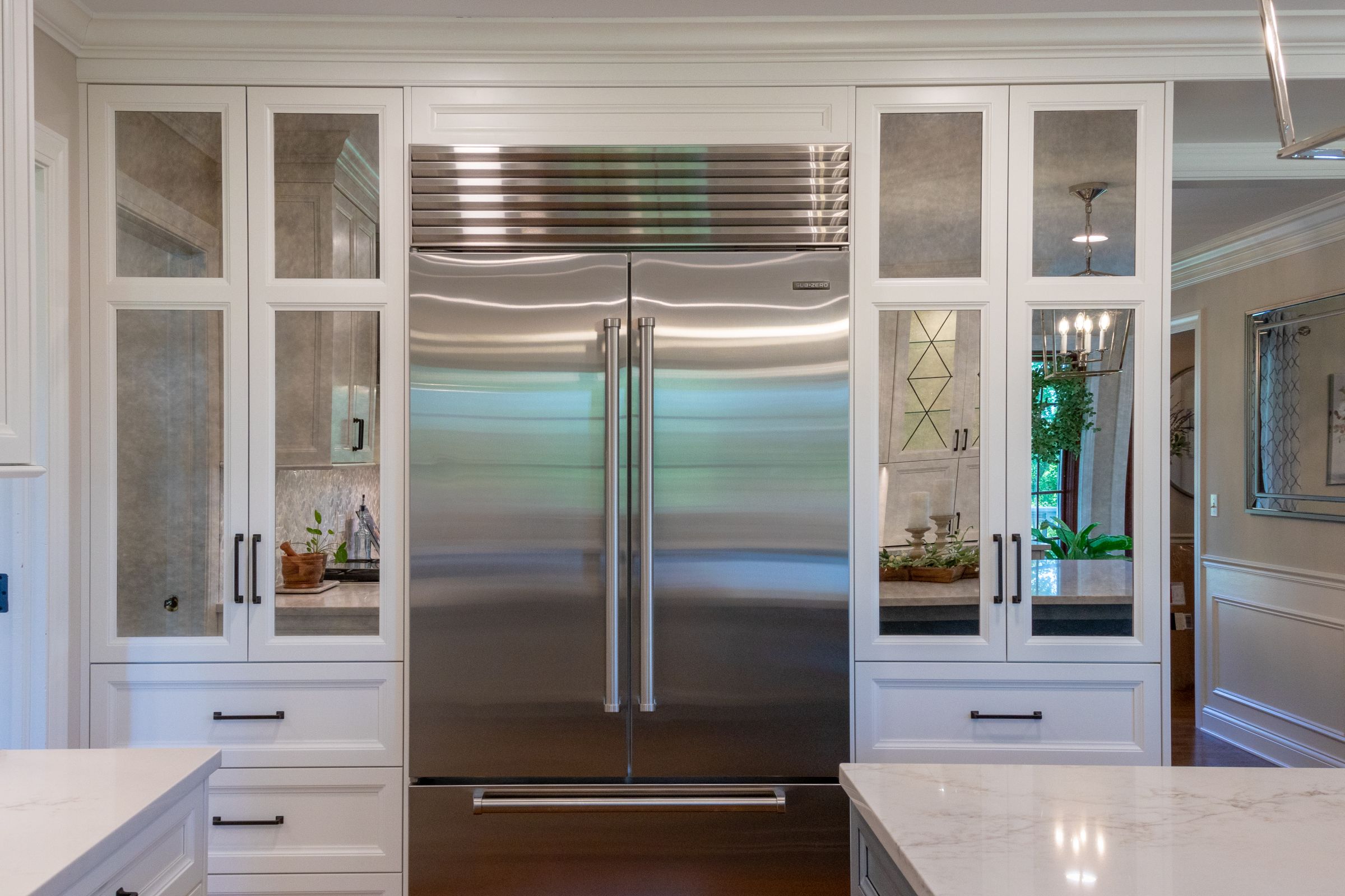 A kitchen with a built-in stainless steel refrigerator flanked by white cabinets with mirrored doors and a white countertop in the foreground.