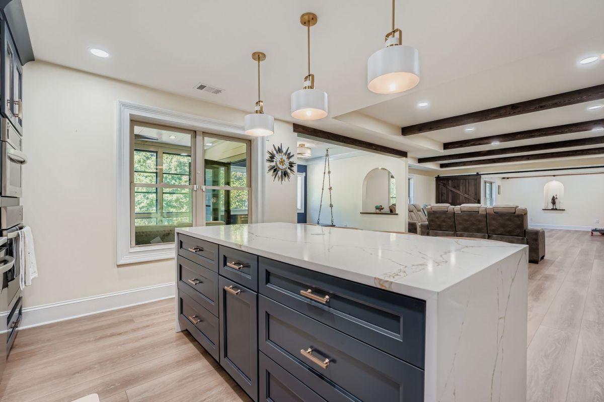 A basement living area with a dark blue kitchen island, light wood floors, and a view into a media room.
