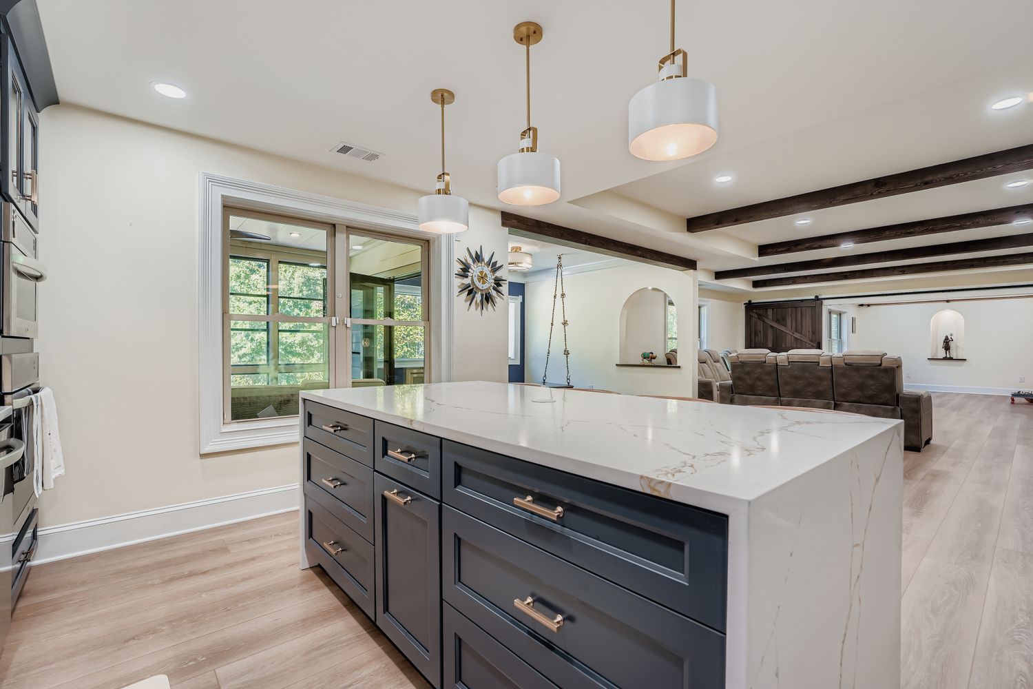 A basement living area with a dark blue kitchen island, light wood floors, and a view into a media room.