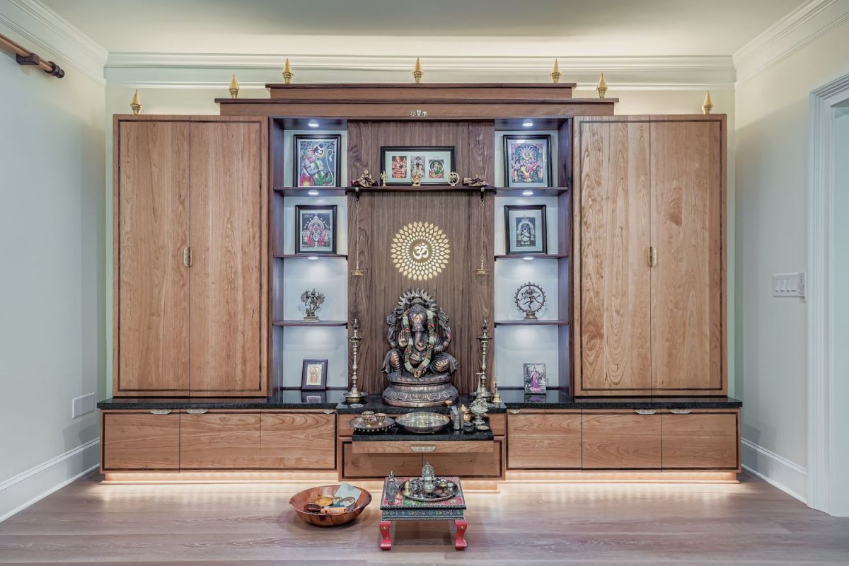 A custom wooden Hindu prayer altar is built into a wall, featuring a large Ganesha statue, various deities, and religious symbols.