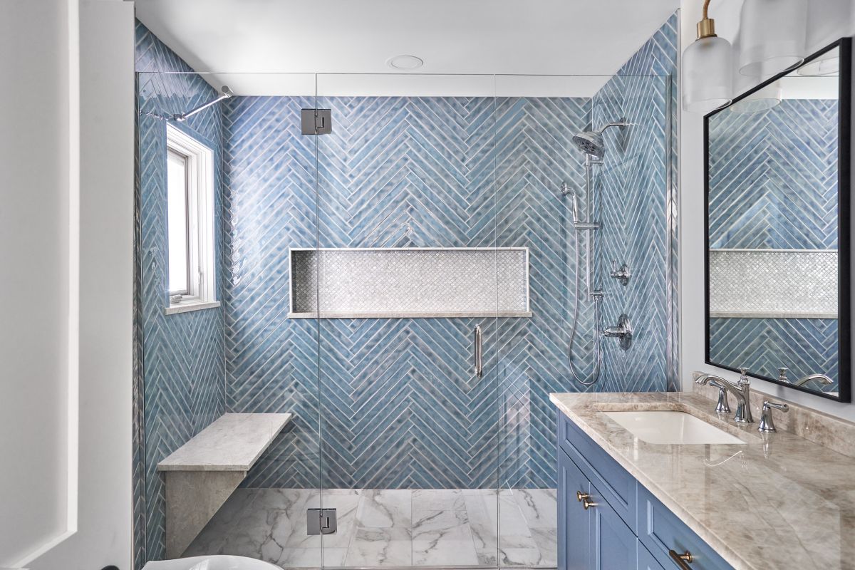 A blue and white bathroom features a walk-in shower with a window, a built-in bench, and a vanity with a sink.