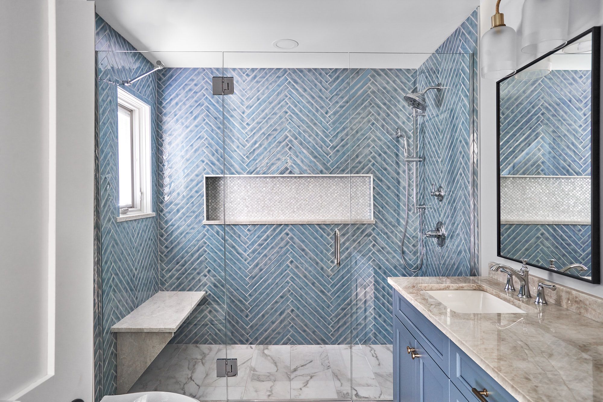 A blue and white bathroom features a walk-in shower with a window, a built-in bench, and a vanity with a sink.