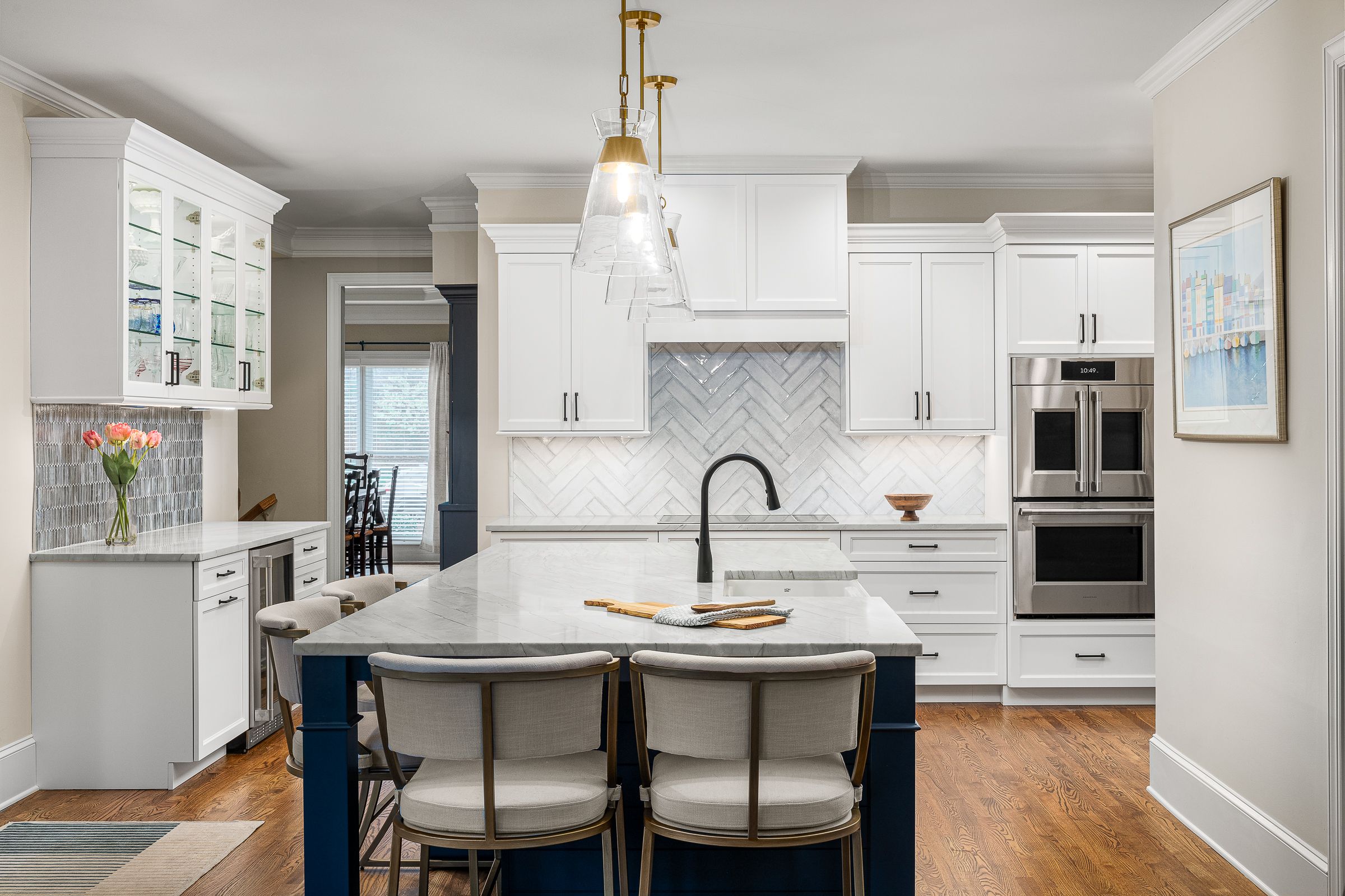 A renovated kitchen features white cabinetry, a large marble island with a dark blue base, and stainless steel appliances.