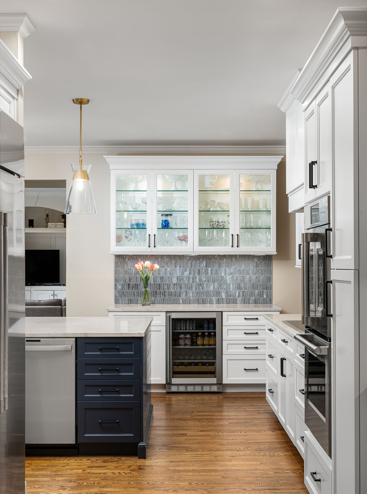 A kitchen with white upper and lower cabinets, a dark blue island, stainless steel appliances, and a gray tiled backsplash.