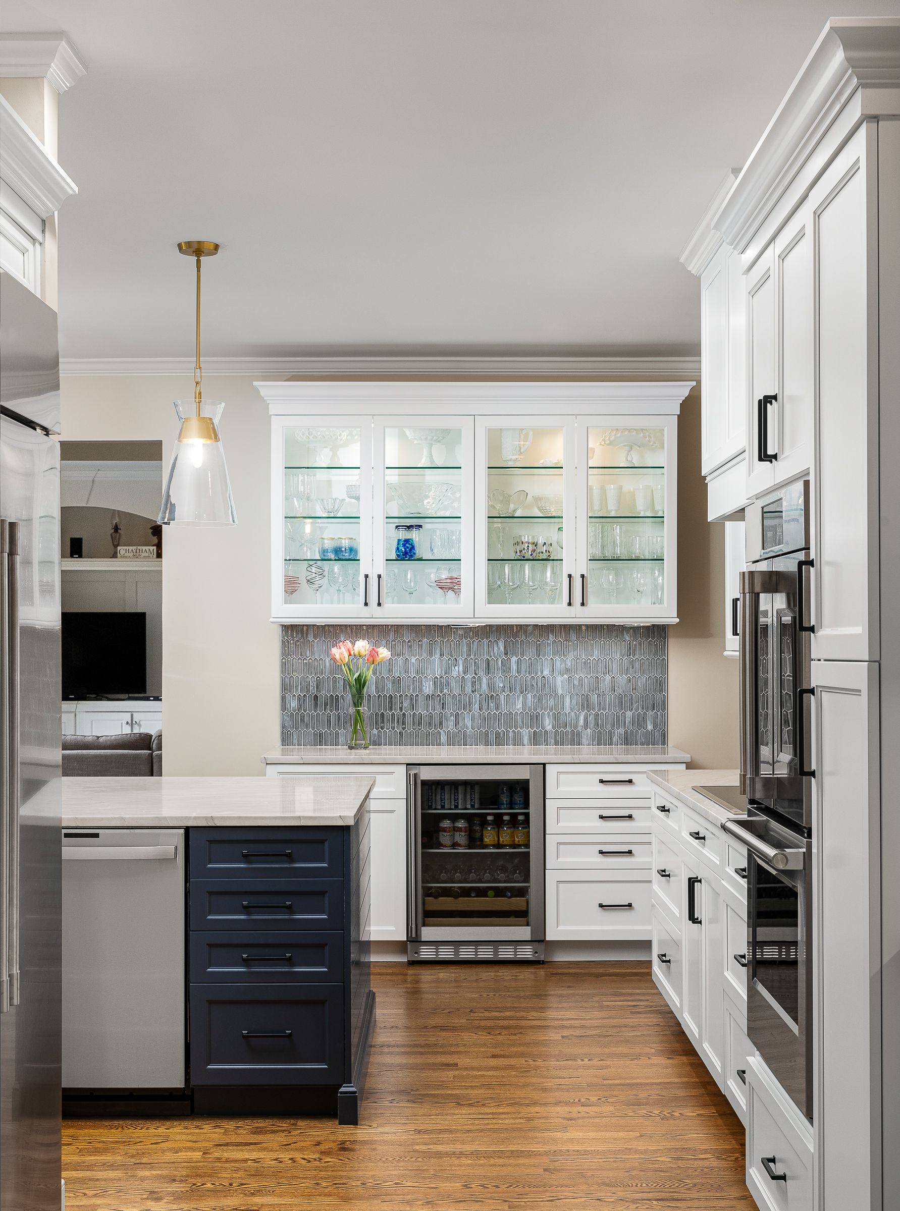 A kitchen with white upper and lower cabinets, a dark blue island, stainless steel appliances, and a gray tiled backsplash.