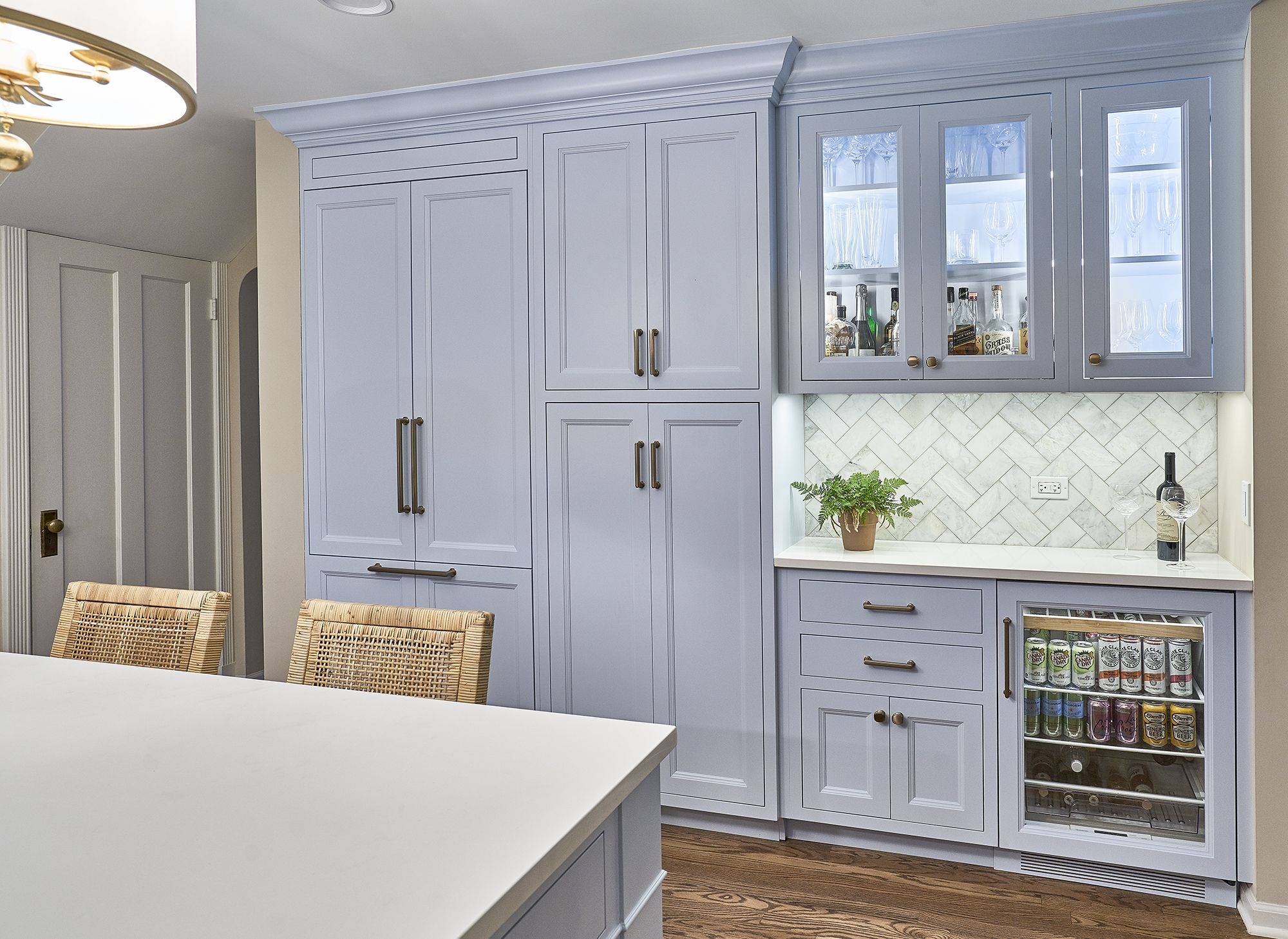 A kitchen with light blue custom cabinetry, a built-in refrigerator, a wet bar with a beverage cooler, and a white countertop.