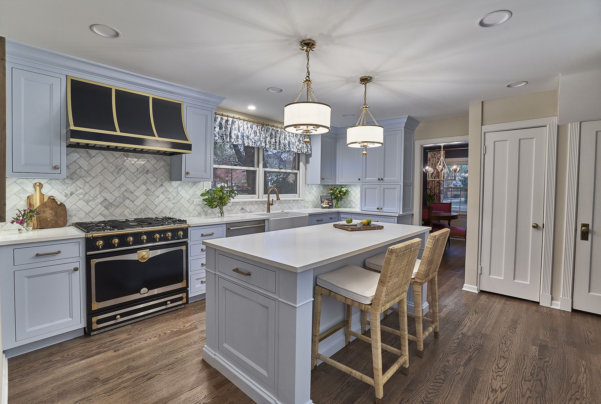 A light blue kitchen with a large island, a black and gold range, and dark wood floors.