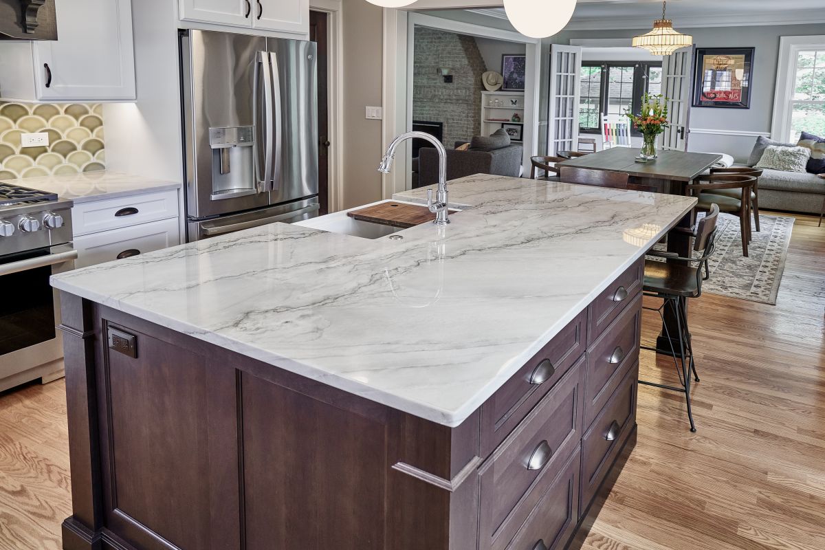 A kitchen with a large island, a stainless steel refrigerator, a range, and a dining area with a table and chairs.
