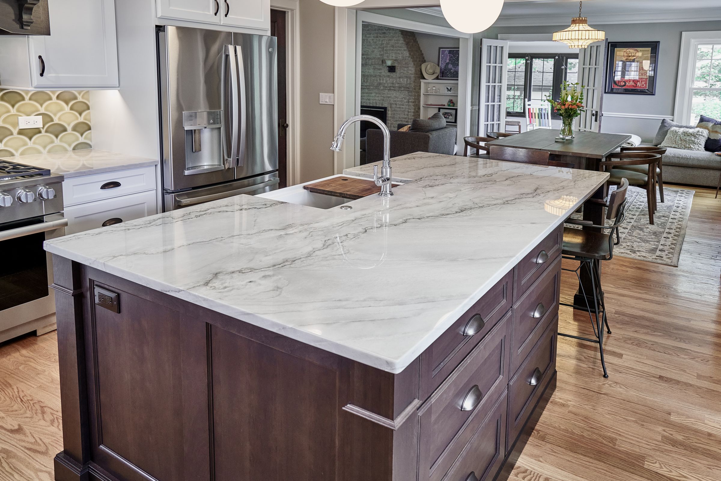 A kitchen with a large island, a stainless steel refrigerator, a range, and a dining area with a table and chairs.
