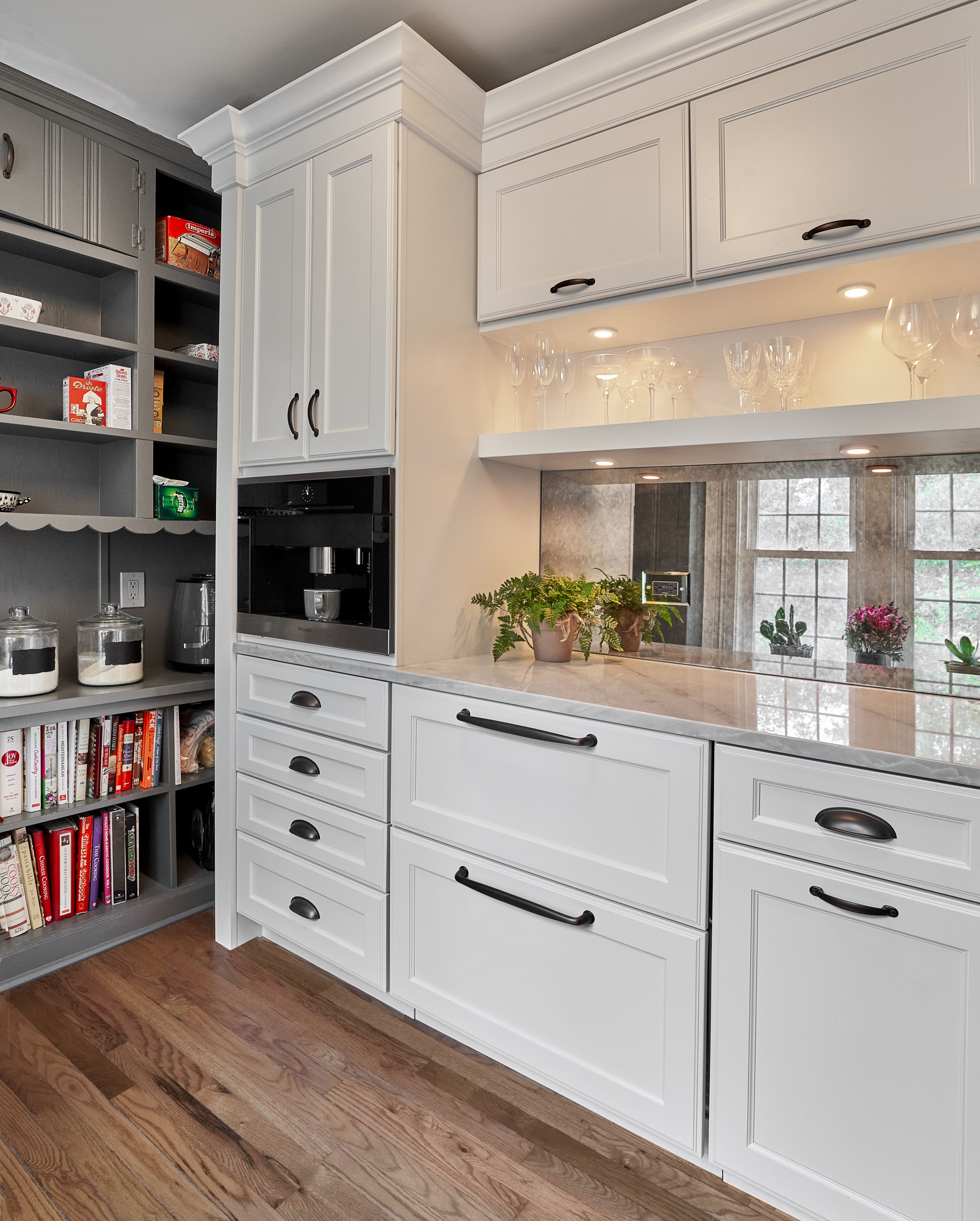 A kitchen features white cabinetry, a built-in coffee maker, open shelving with glassware, and a mirrored backsplash.