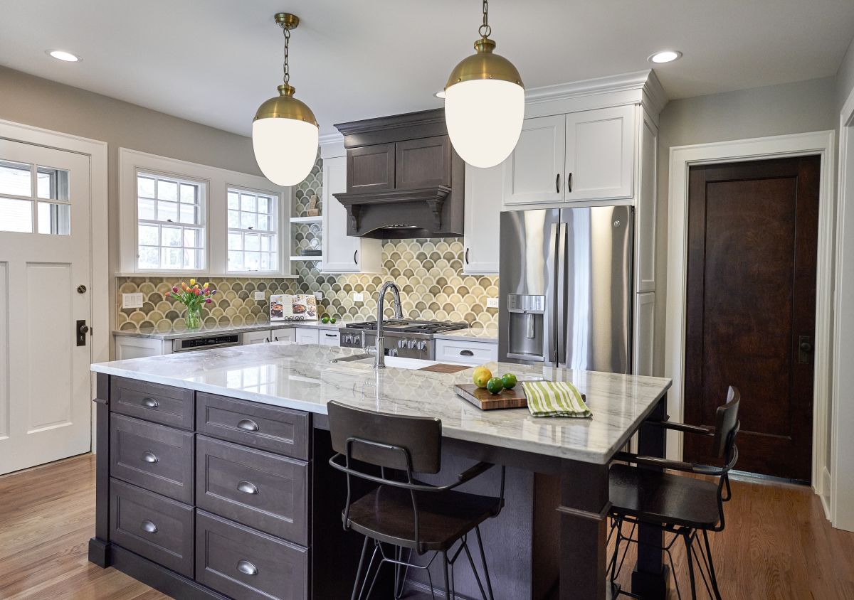 A kitchen features a large island with seating, dark wood cabinets, white upper cabinets, and a patterned backsplash.