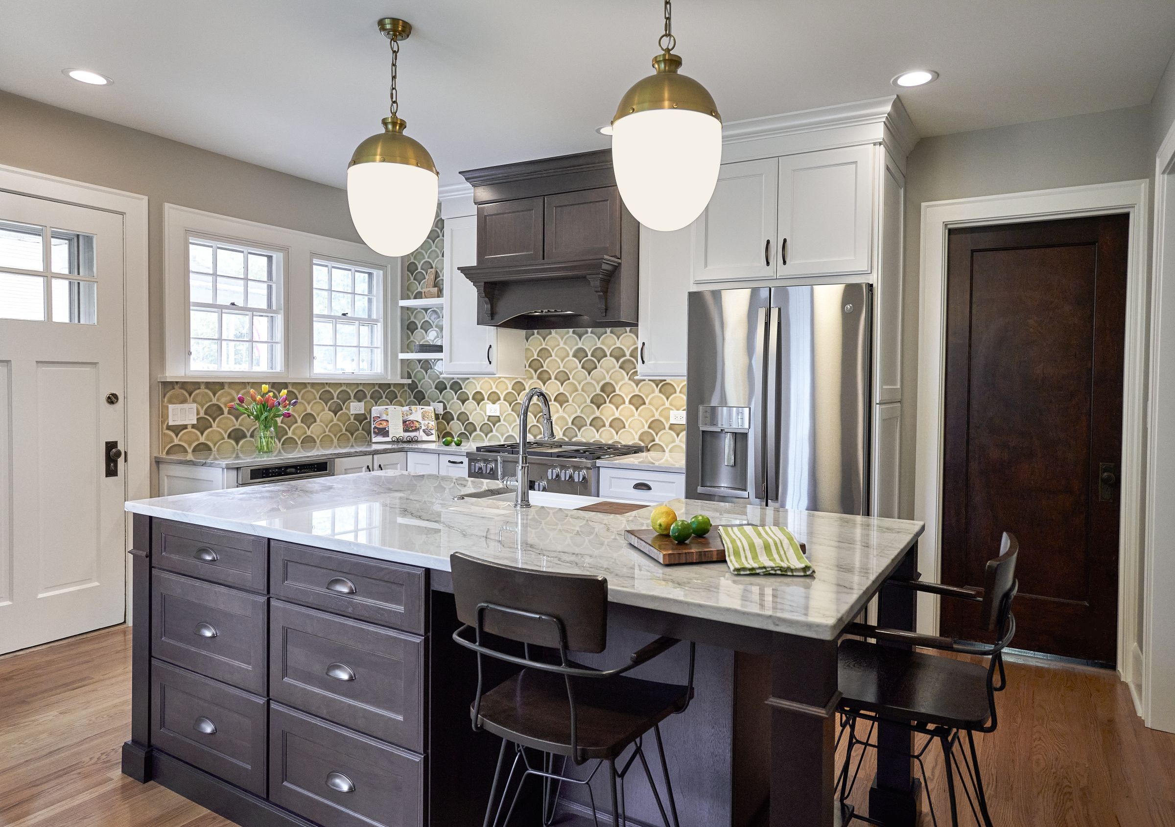A kitchen features a large island with seating, dark wood cabinets, white upper cabinets, and a patterned backsplash.