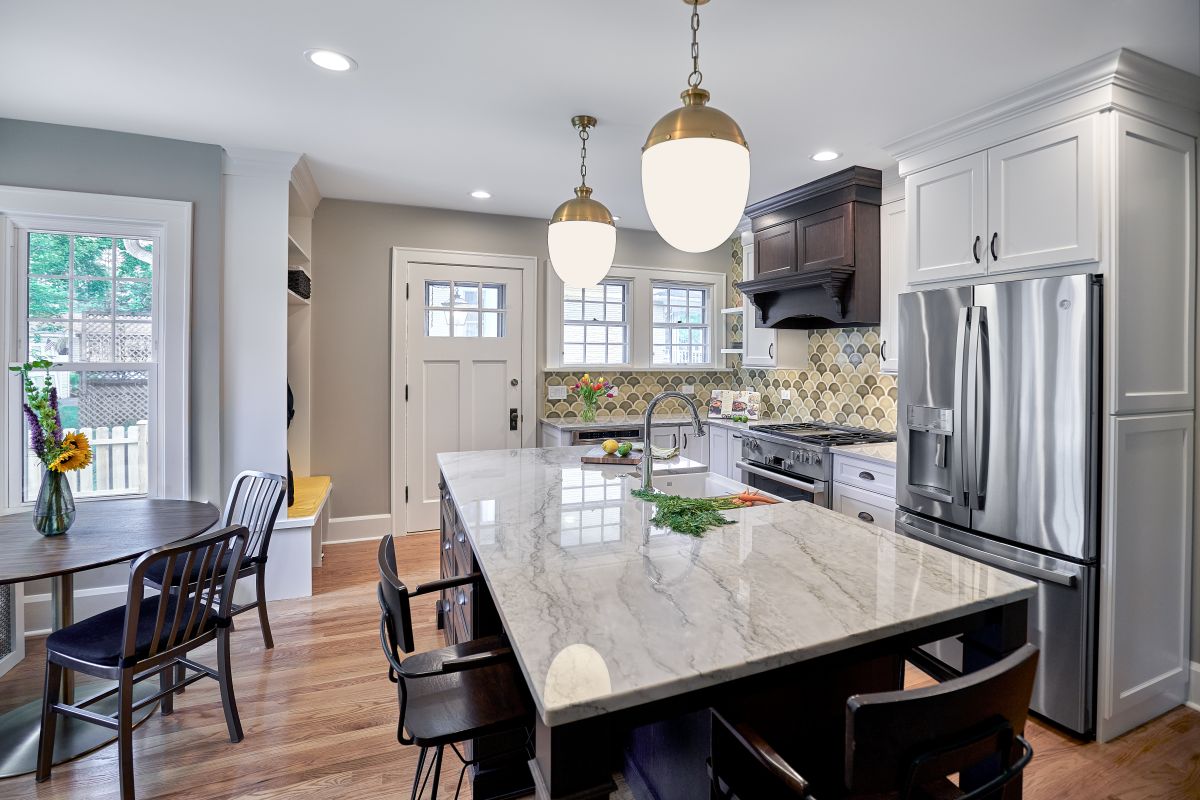 A kitchen with a large central island, a dining area by a window, and a stainless steel refrigerator.