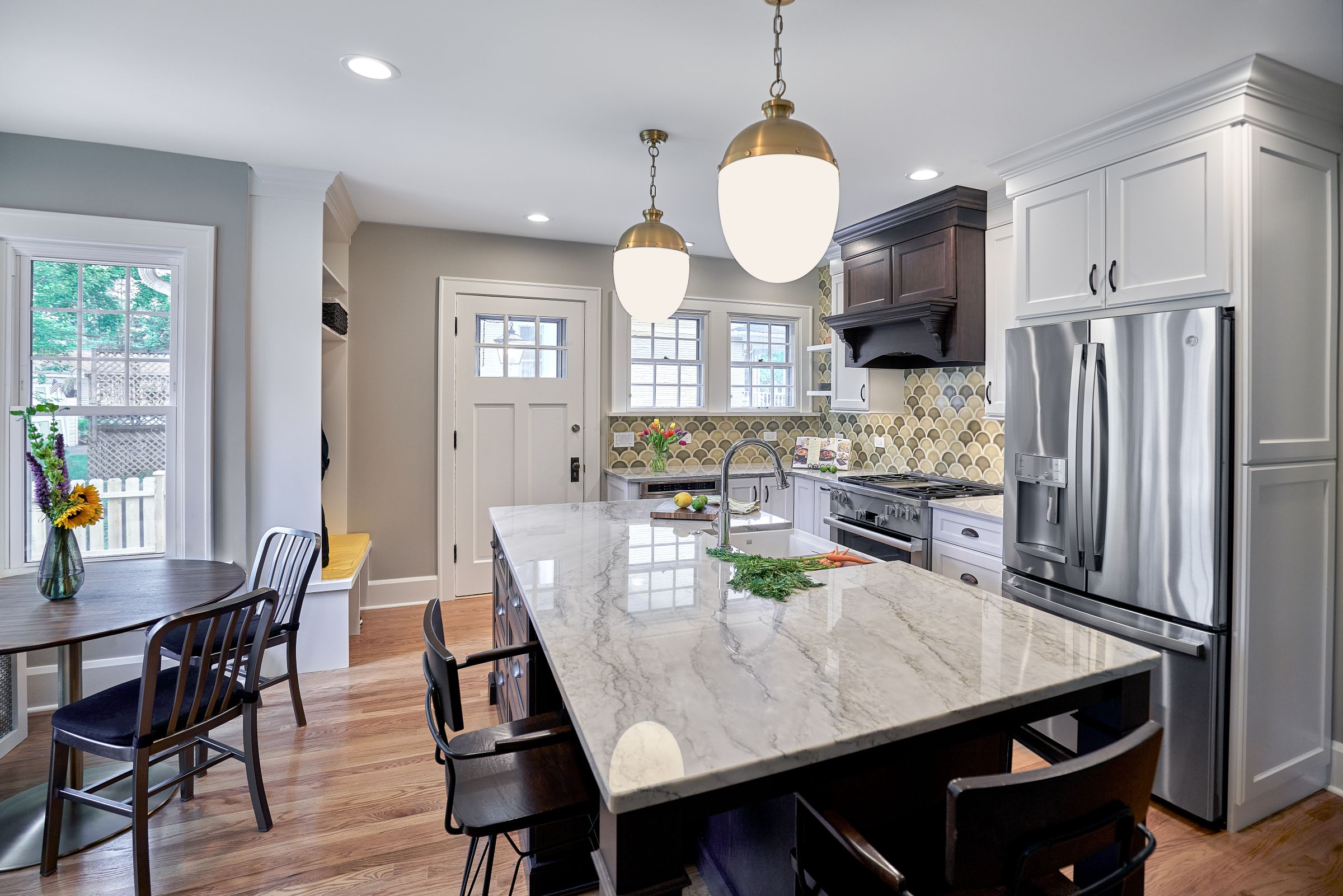 A kitchen with a large central island, a dining area by a window, and a stainless steel refrigerator.