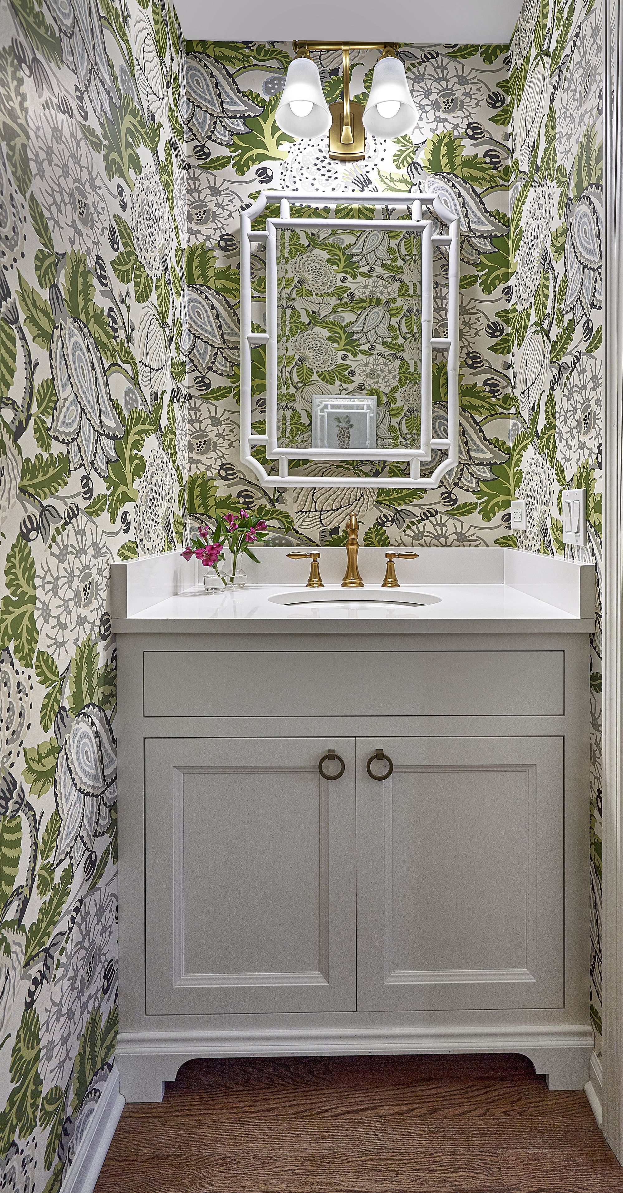 A small bathroom features a vanity with a white countertop and a gold faucet, set against floral wallpaper.