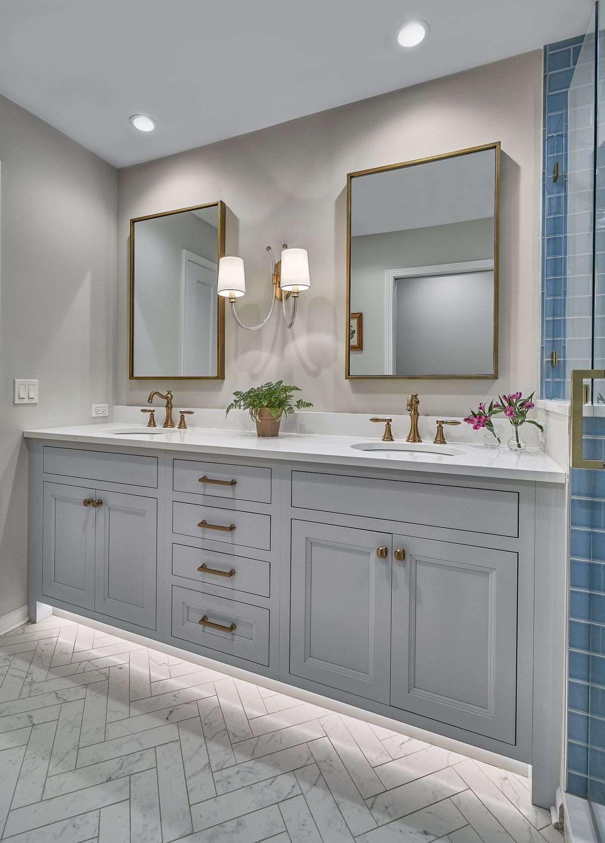 A bathroom features a double vanity with light gray cabinets, white countertops, two mirrors, and brass fixtures.