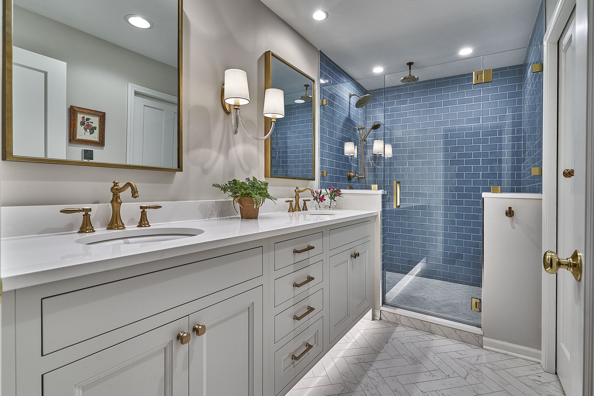 A bathroom with a double vanity, a large mirror, and a walk-in shower with blue subway tiles.
