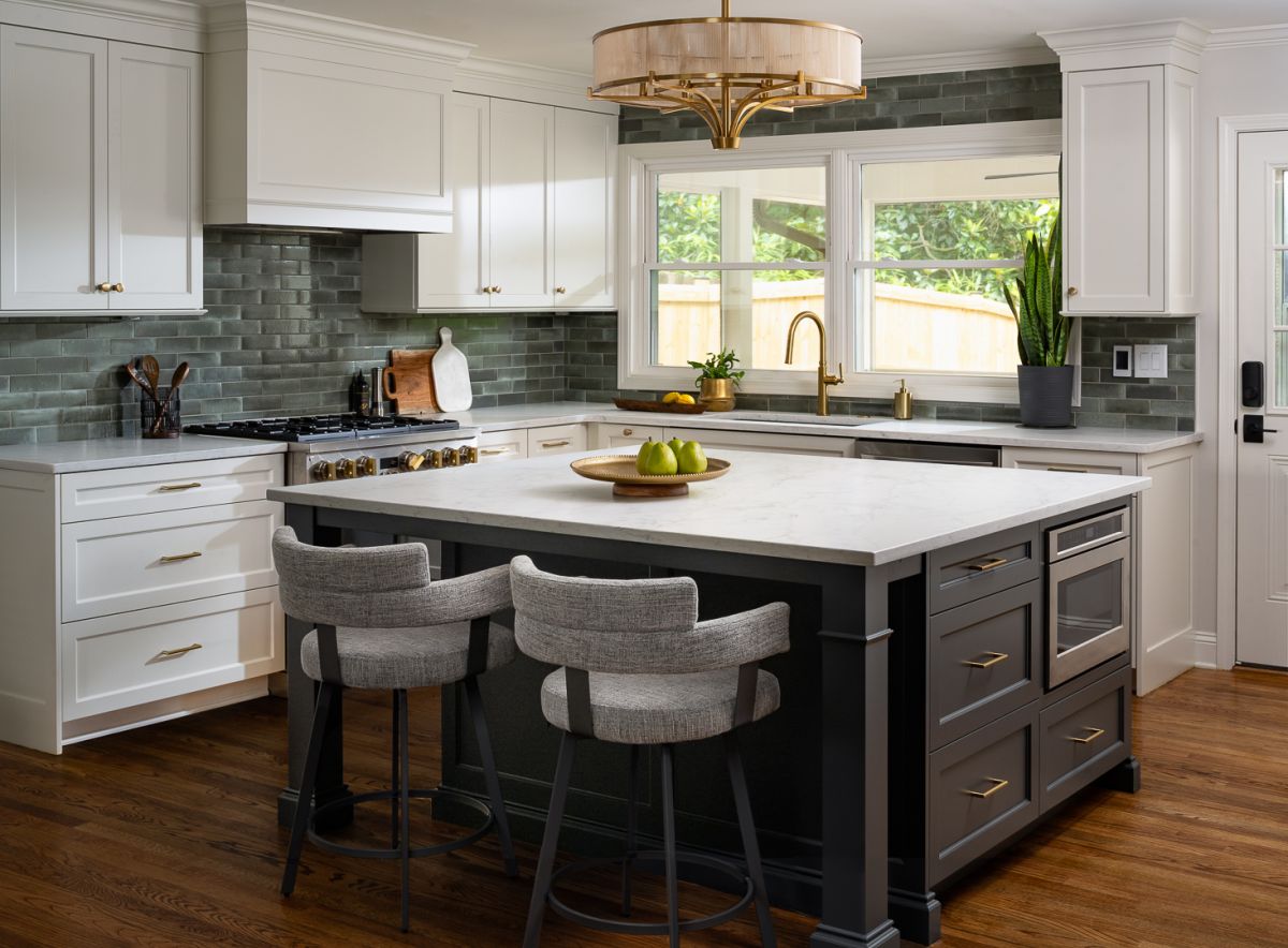 A kitchen with white upper cabinets, a dark gray island with a white countertop, and green subway tile backsplash.