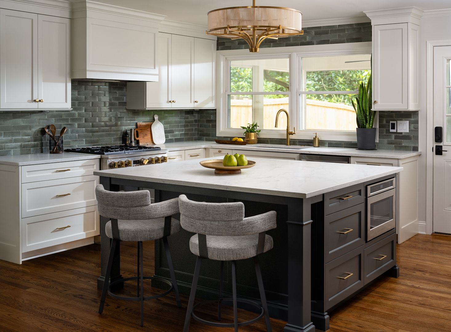 A kitchen with white upper cabinets, a dark gray island with a white countertop, and green subway tile backsplash.