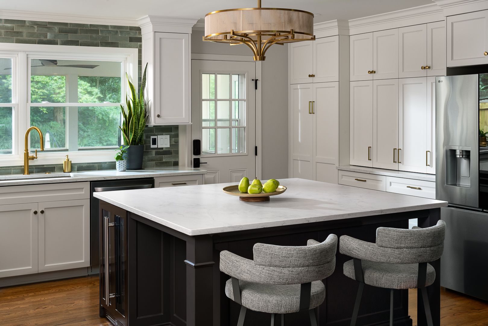 A kitchen with white upper and lower cabinets, a dark island, a large window, and a stainless steel refrigerator.
