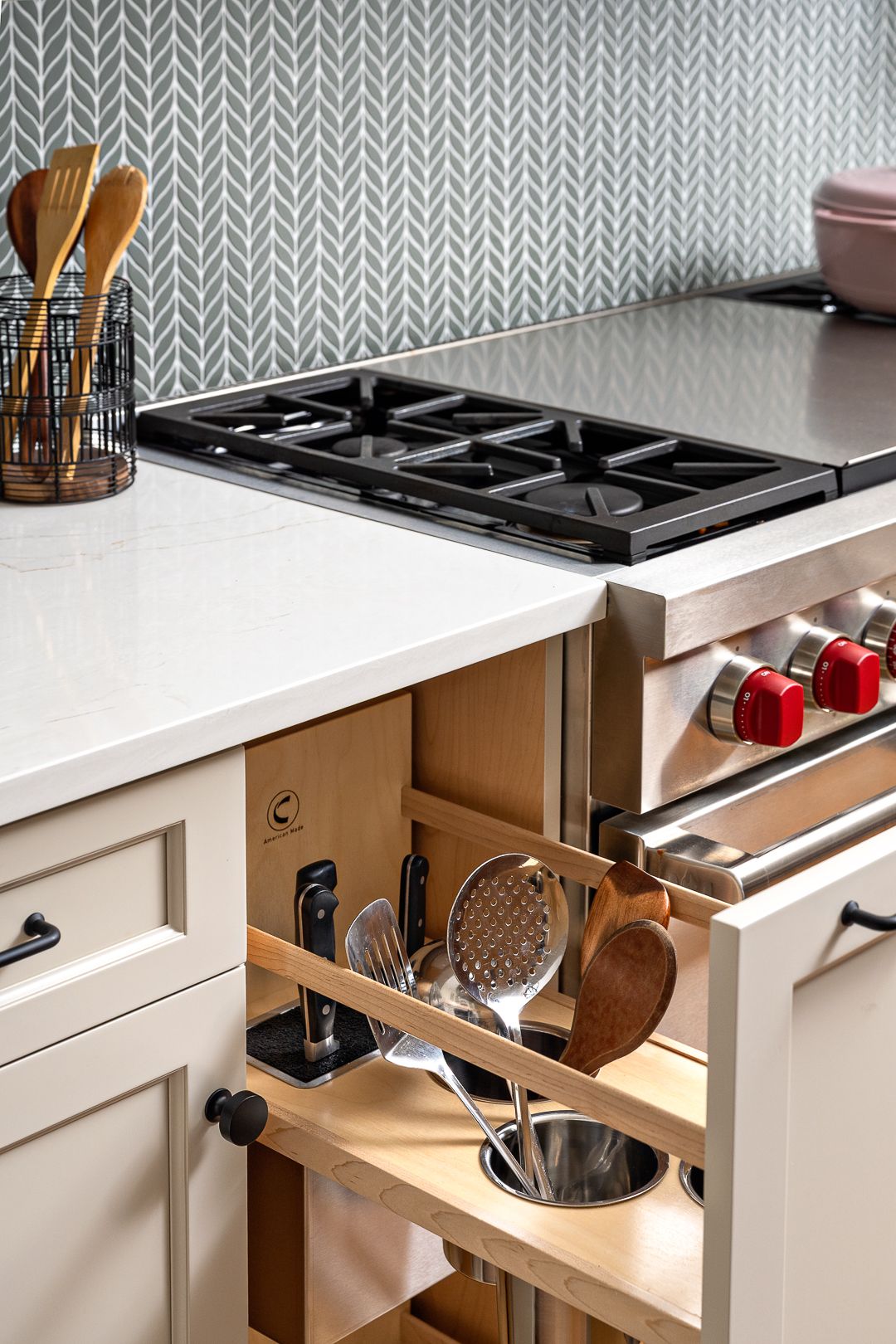 A kitchen features a gas range, light-colored countertops, and a pull-out cabinet with kitchen utensils.