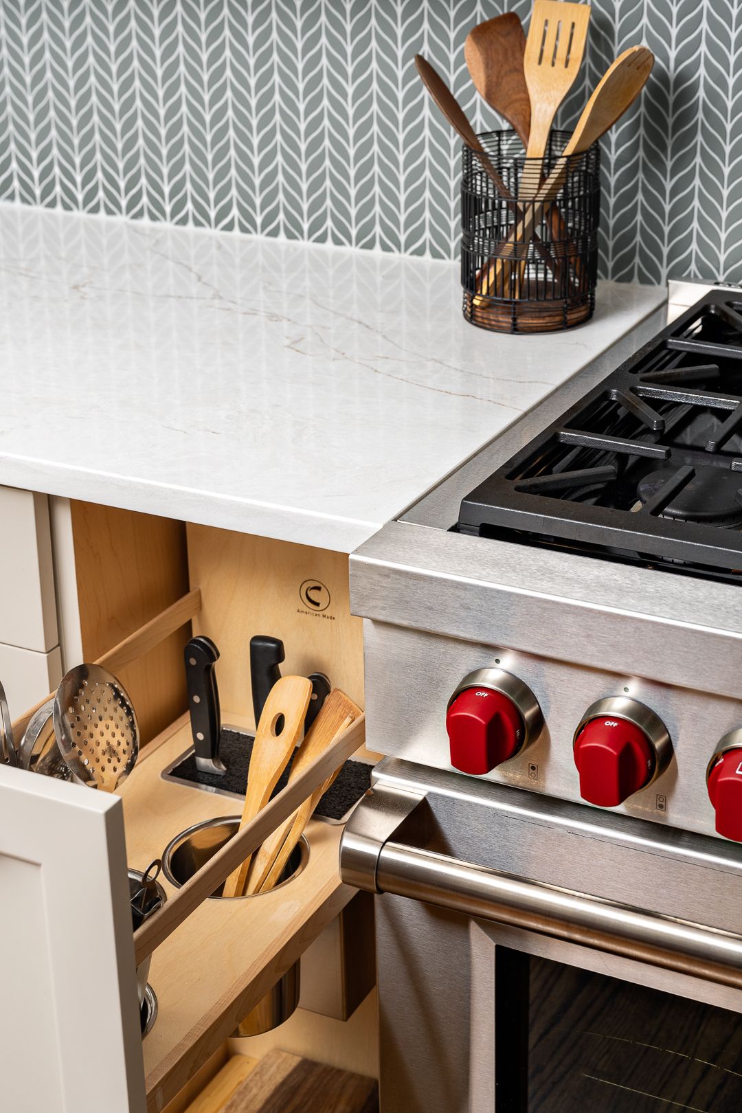 A kitchen with a white countertop, a gray patterned backsplash, a stainless steel range, and an open utensil drawer.