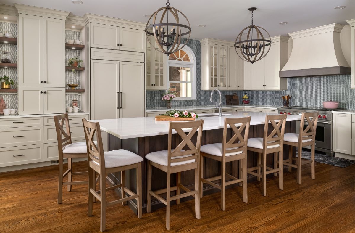 A spacious kitchen features light-colored cabinets, a large island with seating, a refrigerator, a range, and two spherical chandeliers.