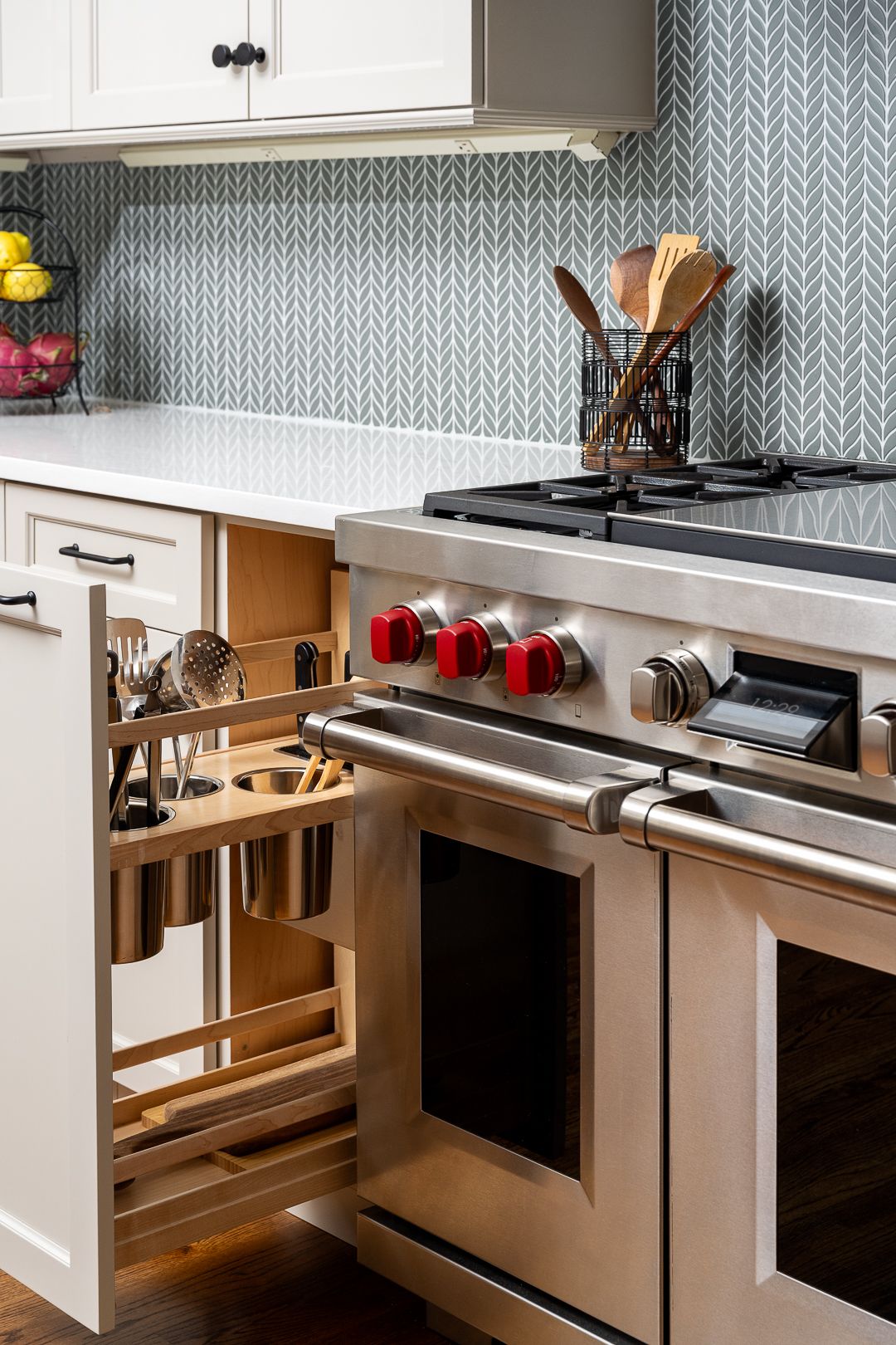 A kitchen features a stainless steel range, white cabinets, light countertop, and a gray patterned backsplash.