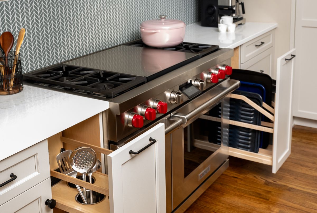 A kitchen features a stainless steel range with red knobs, white countertops, and a gray patterned backsplash.