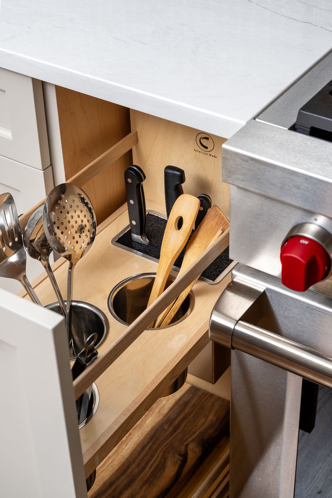 A kitchen drawer with custom wooden organizers for knives, metal utensils, and wooden spatulas, next to a stainless steel range.