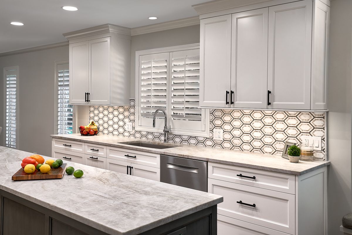 A bright kitchen features white shaker cabinets, a light gray countertop, and a hexagonal tile backsplash.