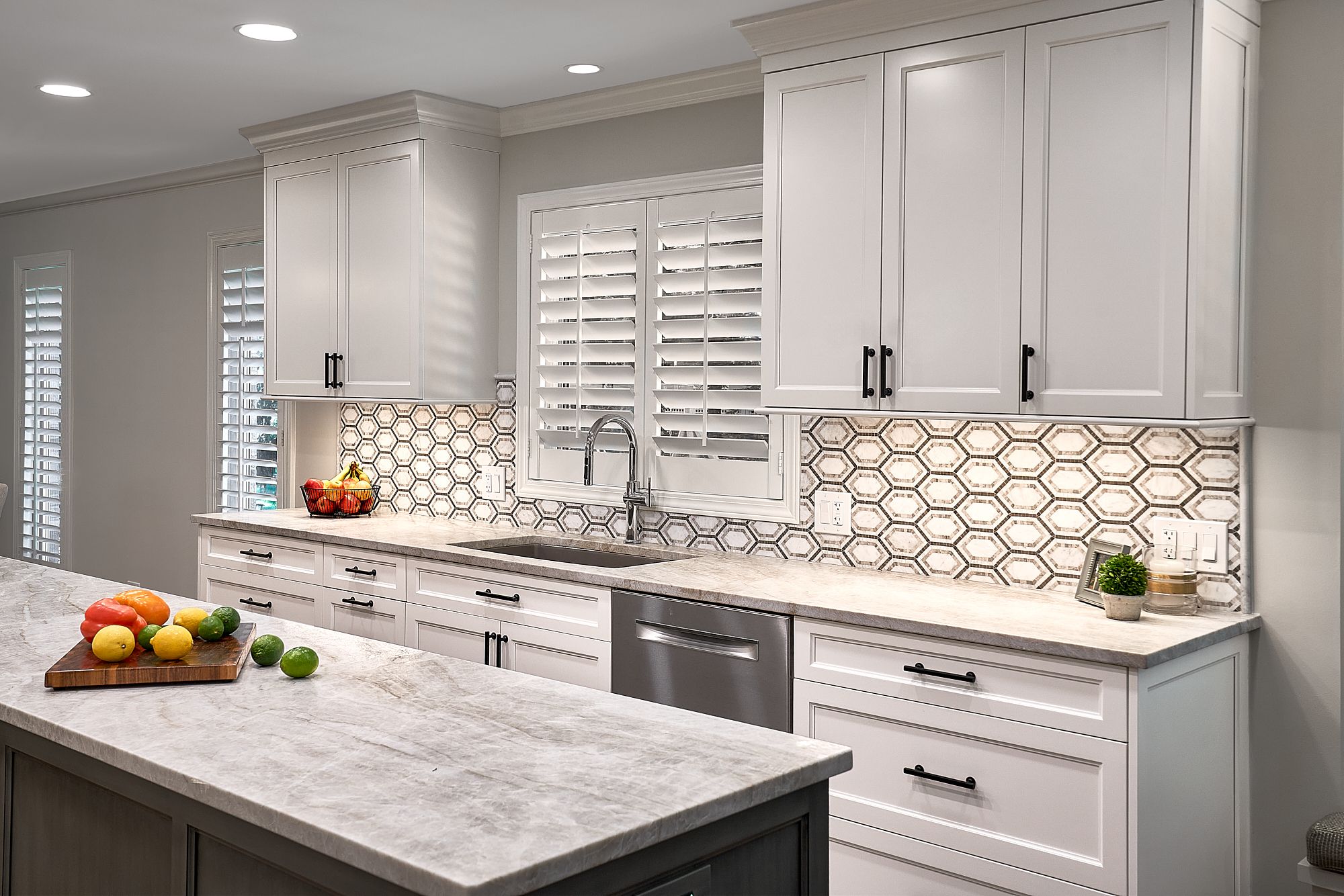 A bright kitchen features white shaker cabinets, a light gray countertop, and a hexagonal tile backsplash.