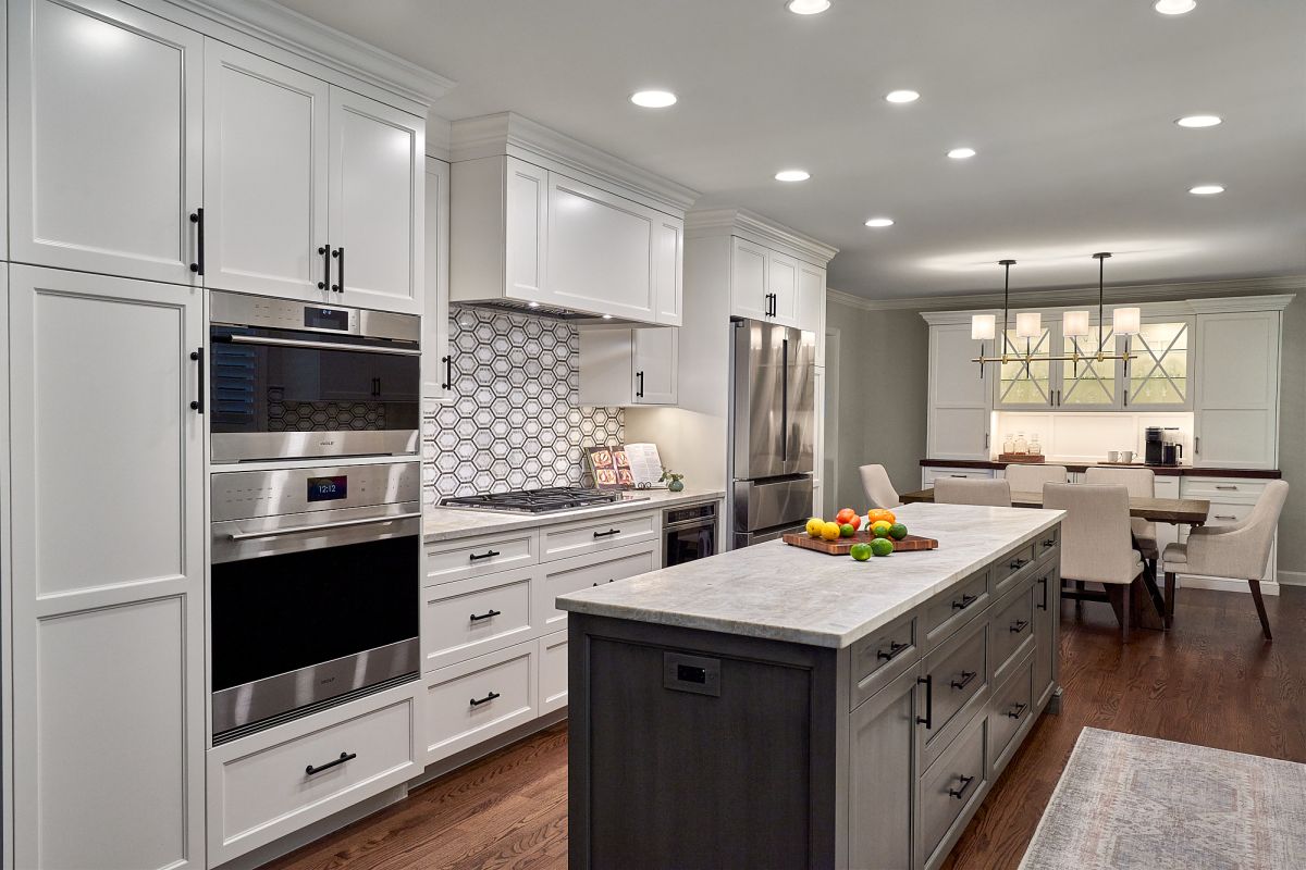 A white kitchen with a large island, stainless steel appliances, and a dining area with a rectangular table and chairs.