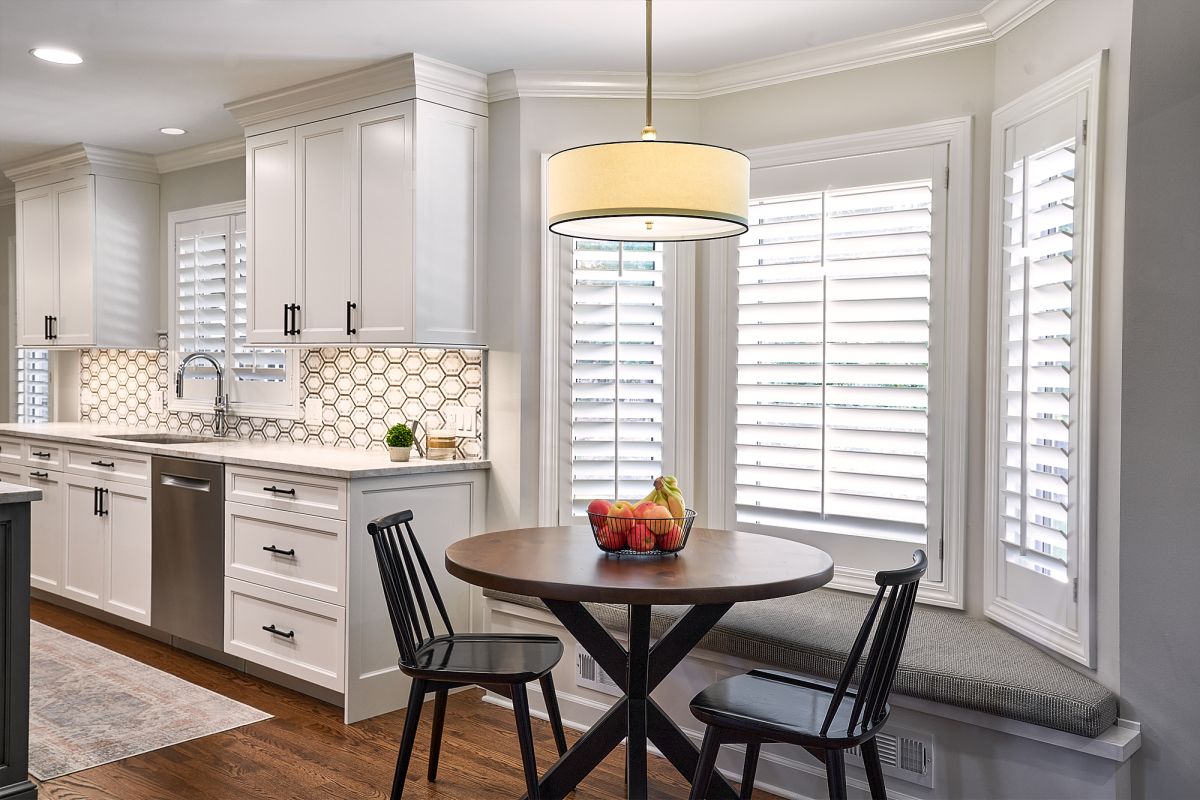 A bright kitchen features white shaker cabinets, a hexagonal tile backsplash, and a breakfast nook with a round table.