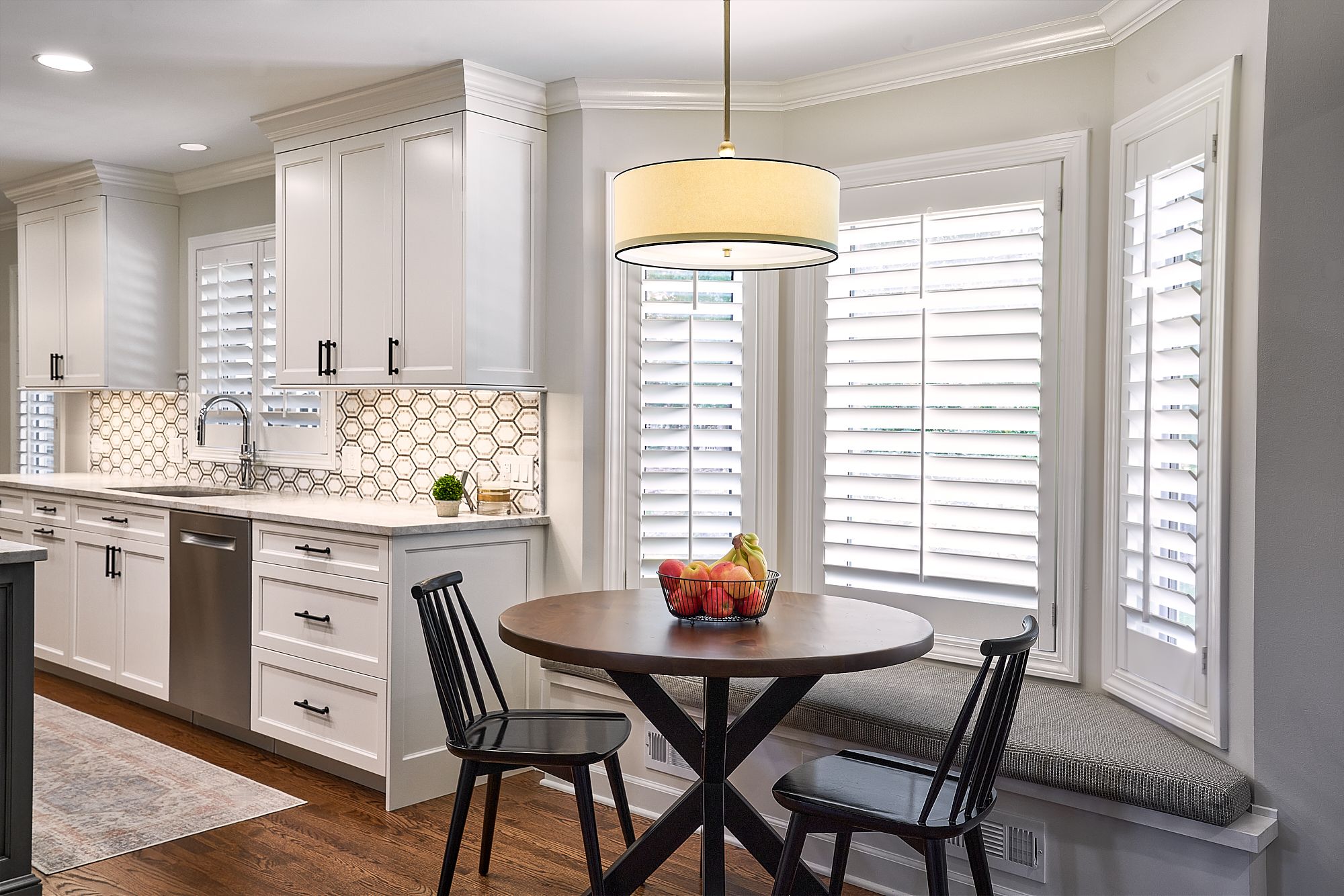 A bright kitchen features white shaker cabinets, a hexagonal tile backsplash, and a breakfast nook with a round table.