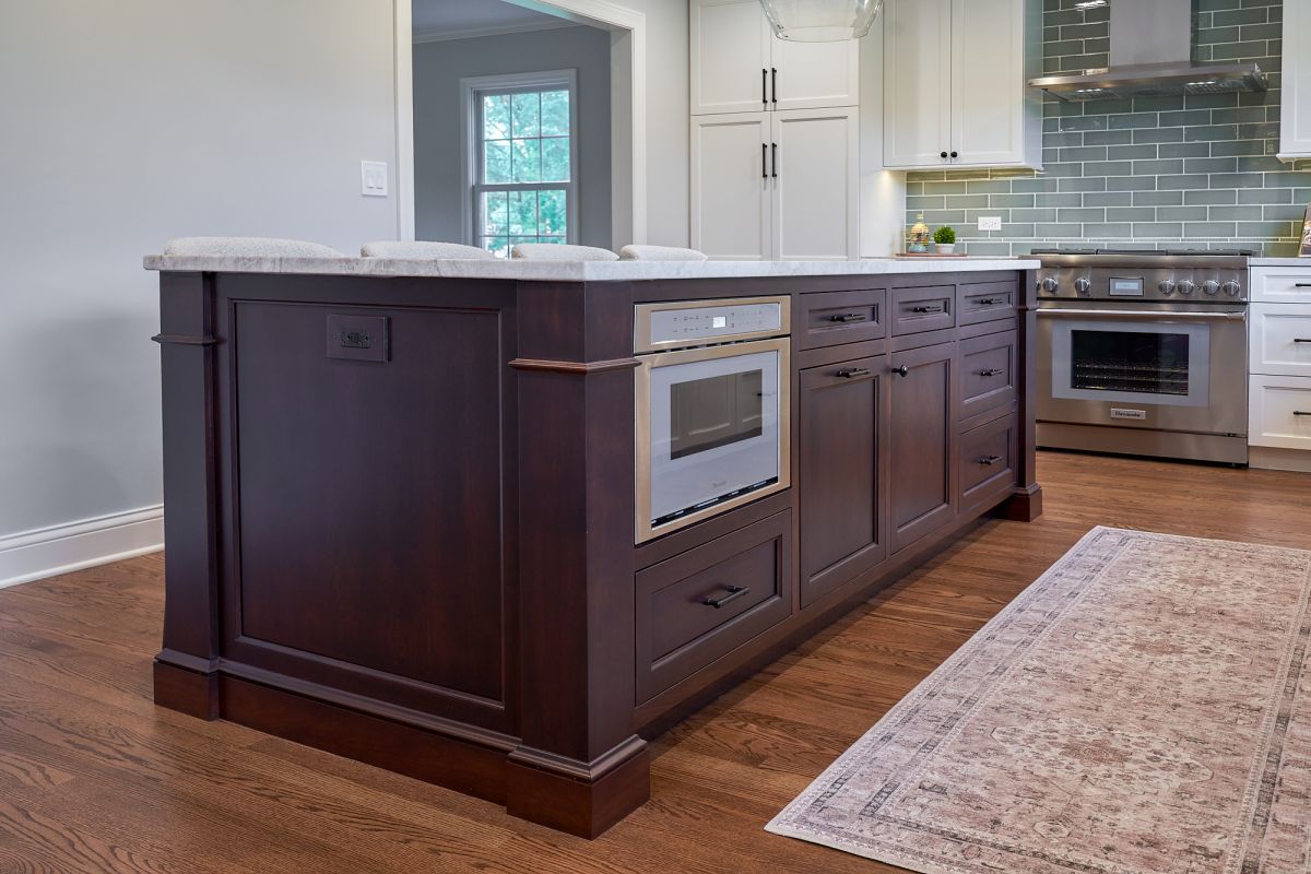 A kitchen features a dark wood island with a built-in microwave, light countertops, and a stainless steel range.