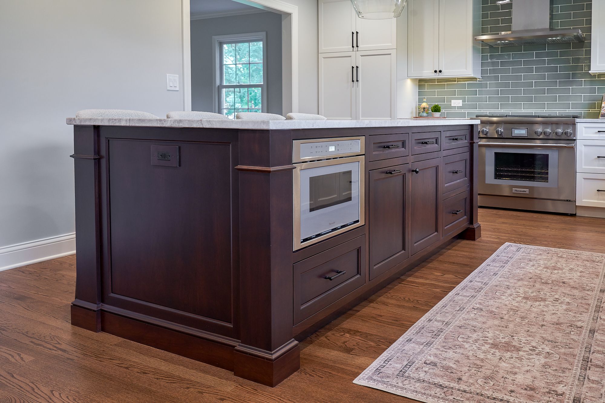 A kitchen features a dark wood island with a built-in microwave, light countertops, and a stainless steel range.