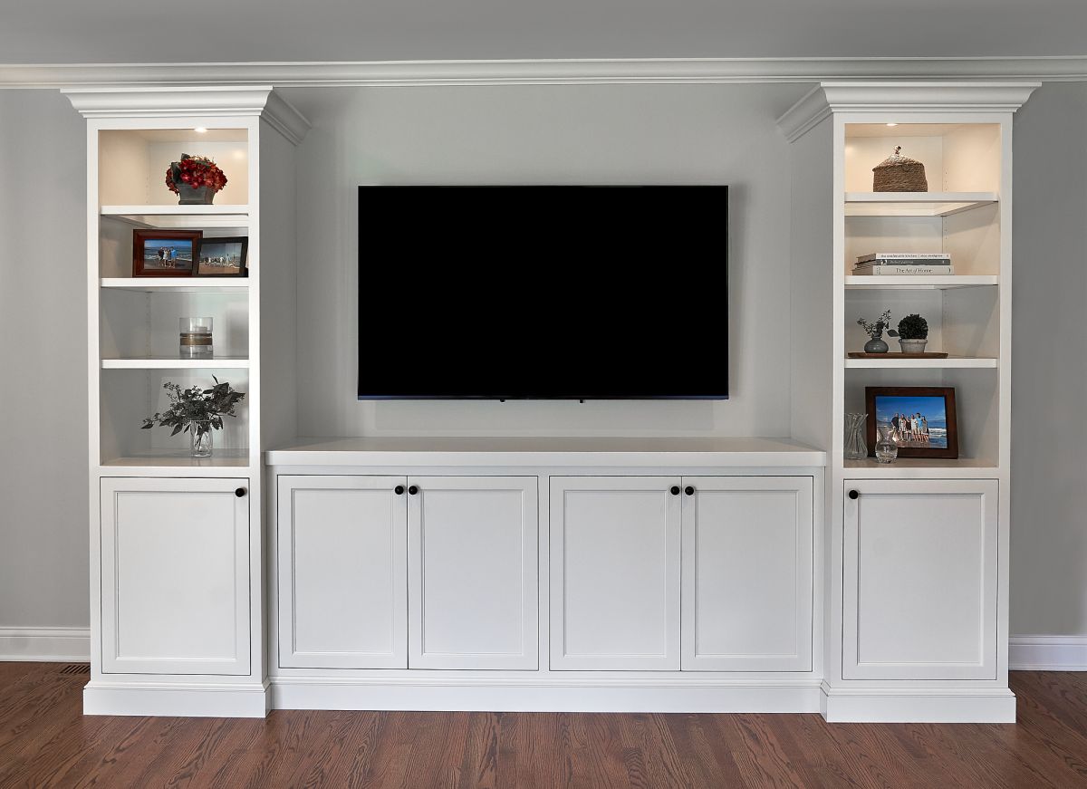 A white built-in entertainment center with a large black television, open shelves, and closed cabinets.