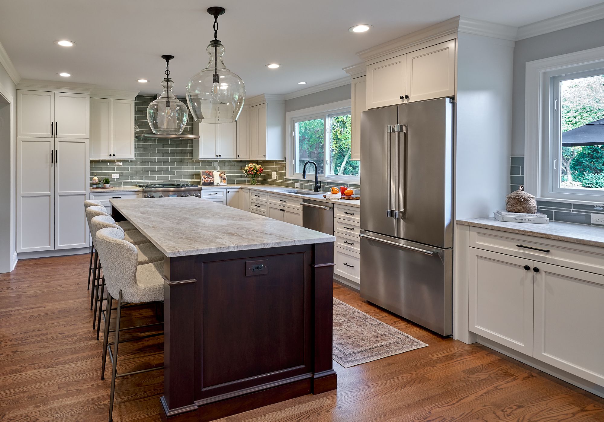 A newly renovated kitchen features white shaker cabinets, a large island with seating, stainless steel appliances, and a green subway tile backsplash.